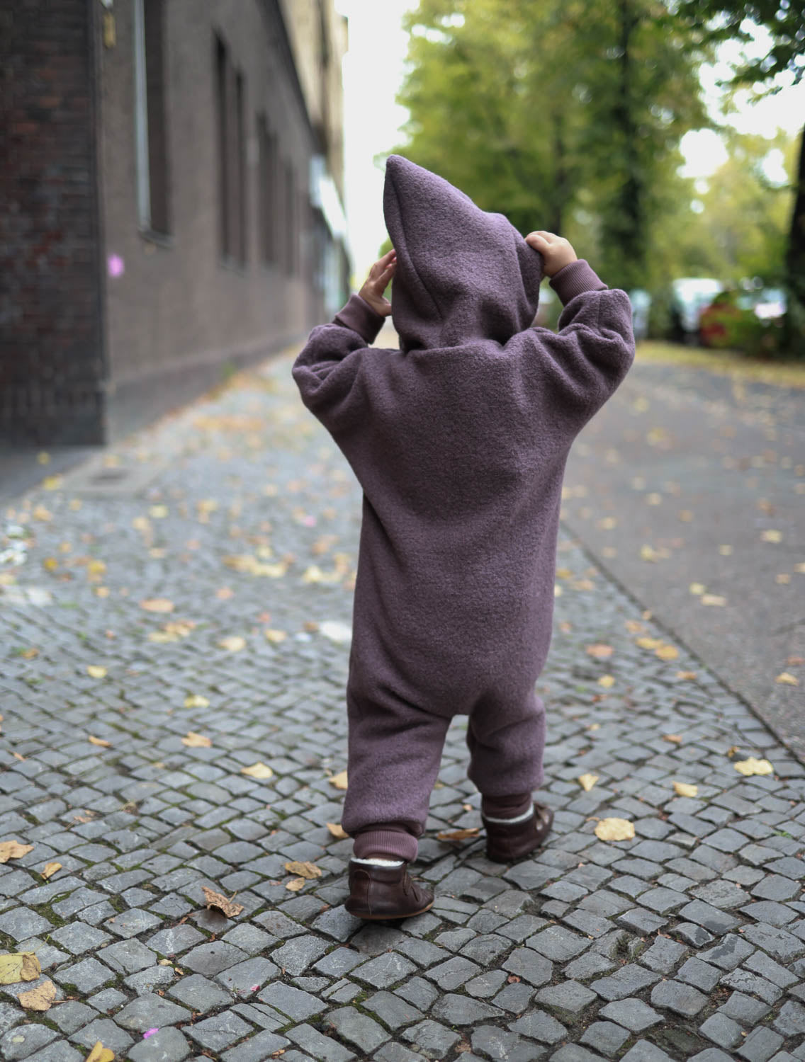 Kleinkind trägt Kuschelanzug Wollwalk - Malve aus Schurwolle mit Bio-Jersey-Futter, ideal für kühle Jahreszeiten. Enganliegende Bündchen schützen vor Kälte, während Bewegungsfreiheit erhalten bleibt. Perfekt für Outdoor-Aktivitäten. Wollwalk Anzug