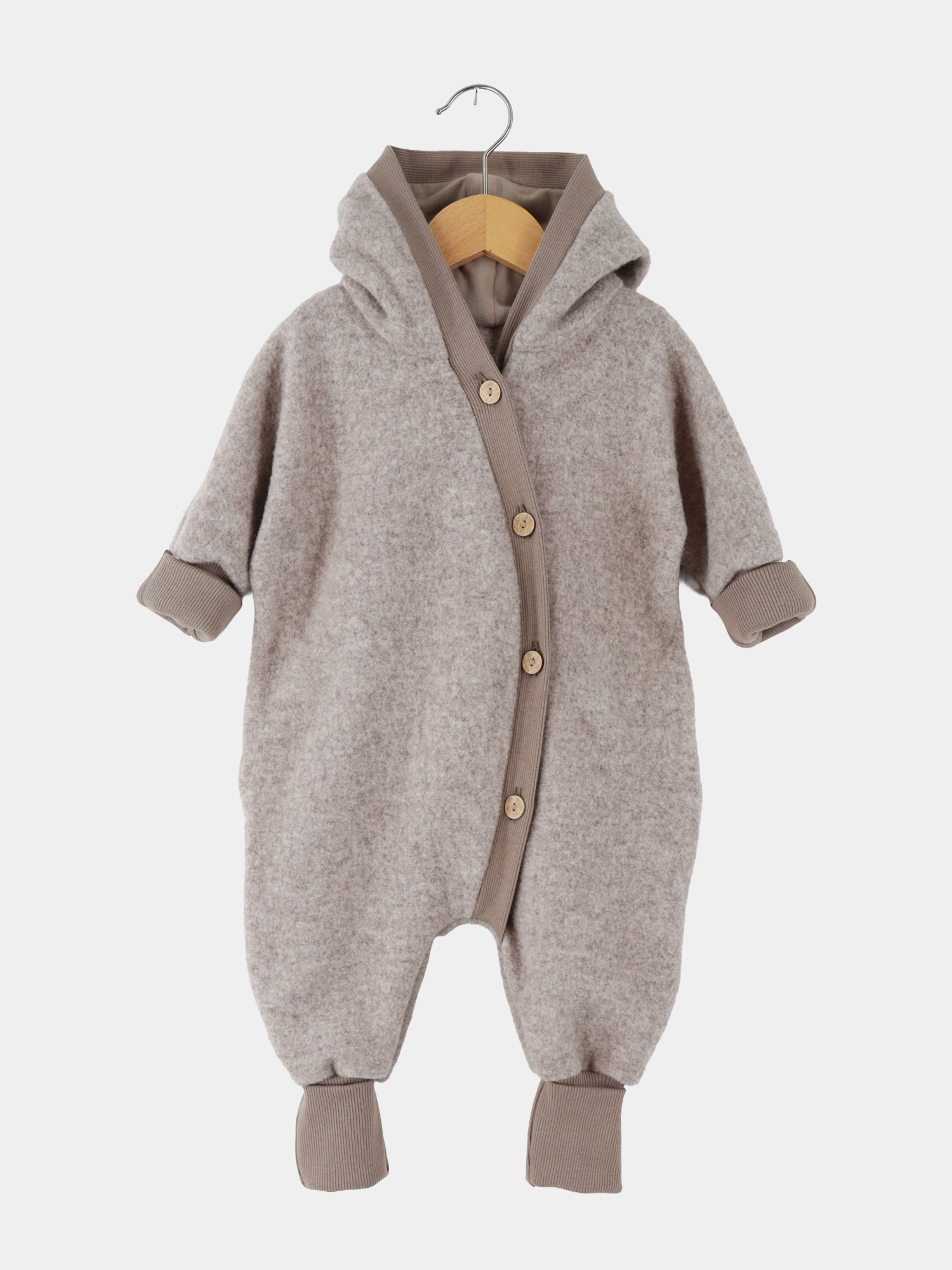 Kuschelanzug Merino Wollfleece - Hafer: Weicher, beigefarbener Baby-Overall mit Kapuze aus Merino-Wollfleece, diagonal angeordnete Holzknöpfe, gerippte Bündchen an Ärmeln und Beinen, auf Holzkleiderbügel präsentiert.
