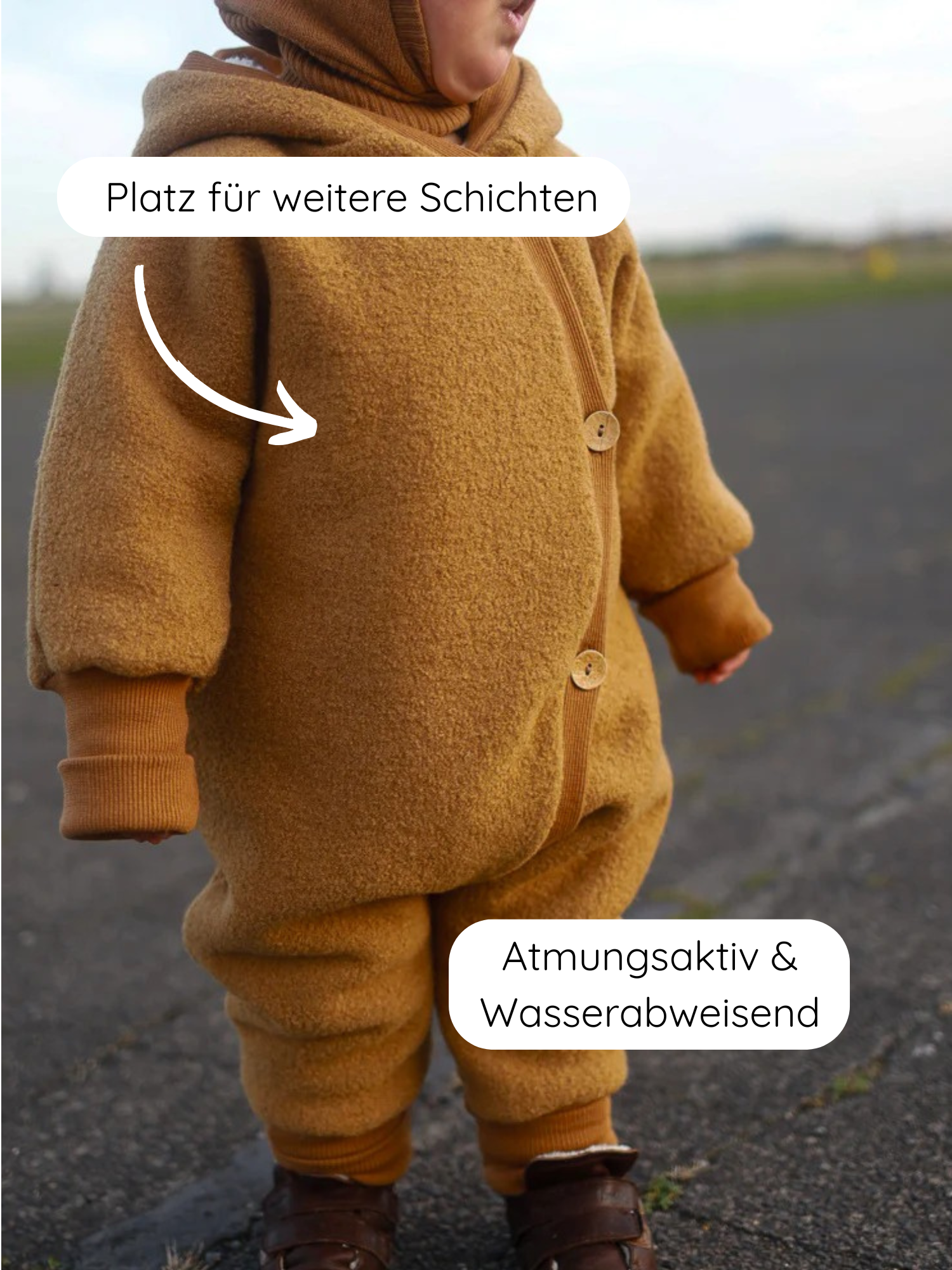 Kleinkind im Wollwalk Overall mit Teddyfutter - Honig, mit Kapuze und Holzknöpfen. Pfeile zeigen Eigenschaften: Platz für weitere Schichten am Oberkörper, Atmungsaktiv & Wasserabweisend an den Beinen.