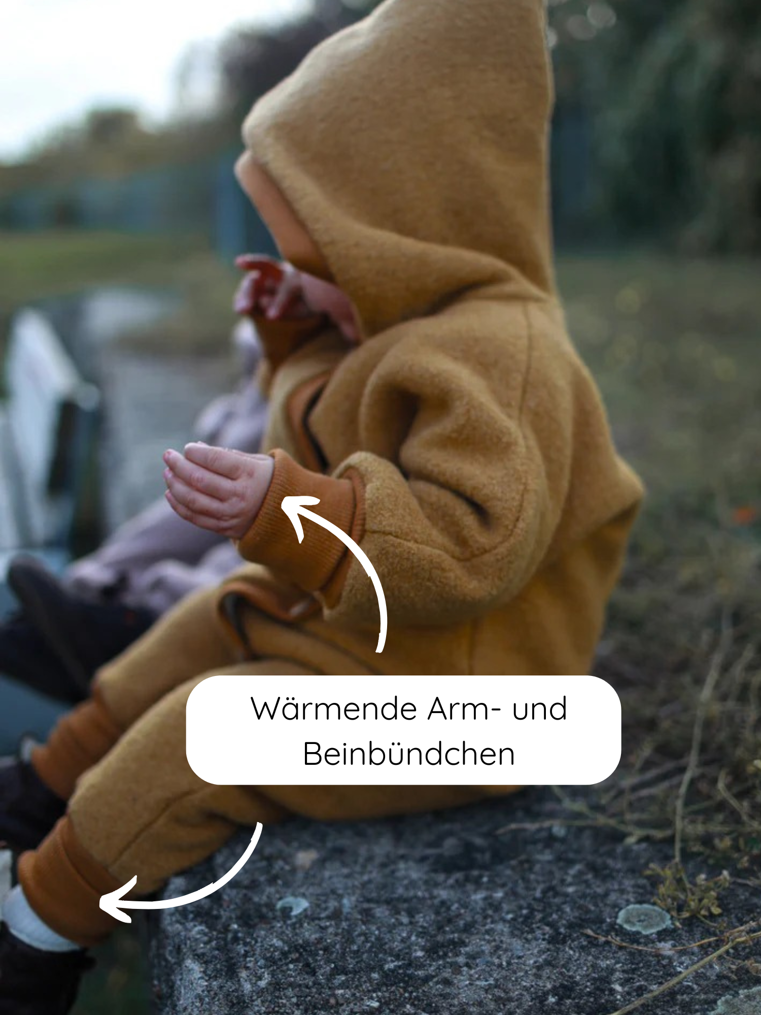 Kleinkind sitzt auf Steinmauer, trägt den Winter Wollwalk Overall mit Teddyfutter - Honig. Gezeigt werden die breiten Bündchen an Armen und Beinen, die für Wärme sorgen.