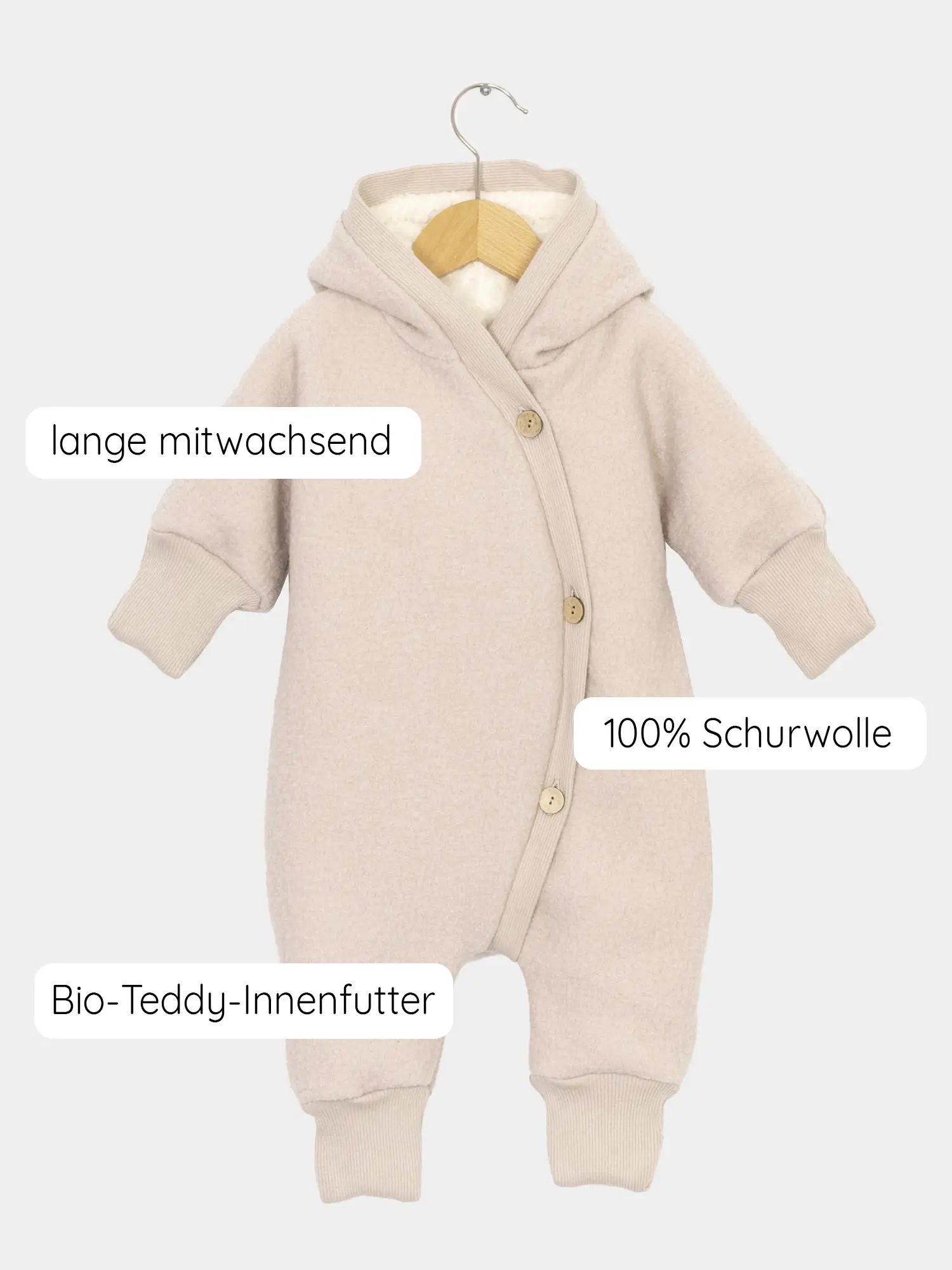 Teddy-Kuschelanzug Wollwalk - Sand: Ein beige Baby-Einteiler aus 100 % Schurwolle mit Bio-Teddy-Innenfutter, langen Mitwachsbündchen, auf einem Holzkleiderbügel hängend. Ideal für kalte, winterliche Tage.