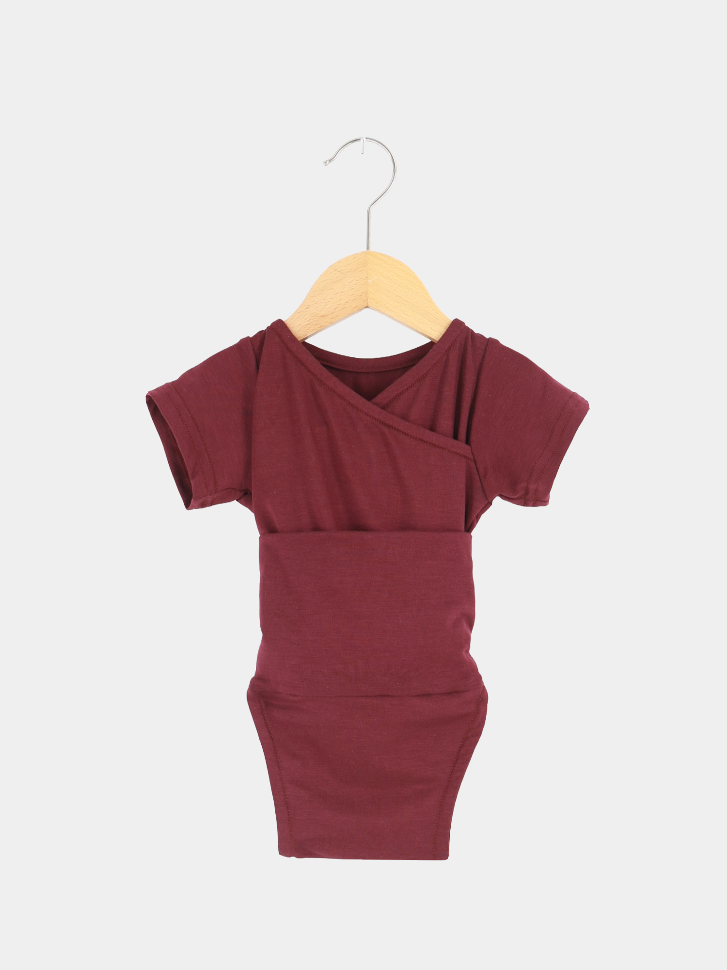 Kurzarm Loopbody Bambusviskose - Burgund, ein kurzärmeliger Baby-Body mit Wickelstil, hängt an einem Holzkleiderbügel. Ideal für warme Tage, bietet Komfort und Bewegungsfreiheit durch atmungsaktive Bambusviskose.