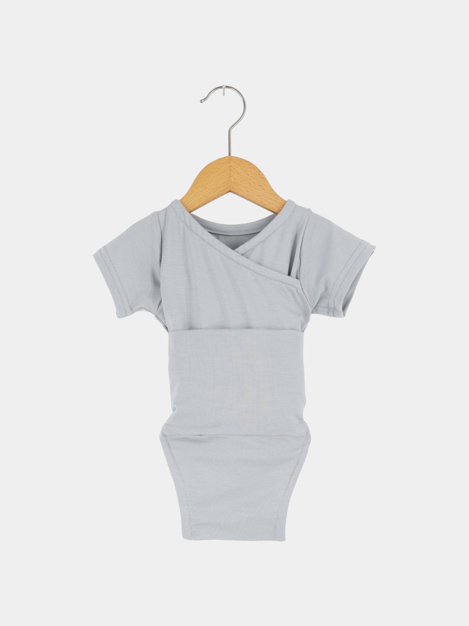 Kurzarm Loopbody Bambusviskose - Eisblau: Ein hellgrauer Kurzarm-Babybody mit kimonoartigem Vorderteil, aus weichem, atmungsaktivem Bambusstoff, hängt an einem kleinen Holzbügel.