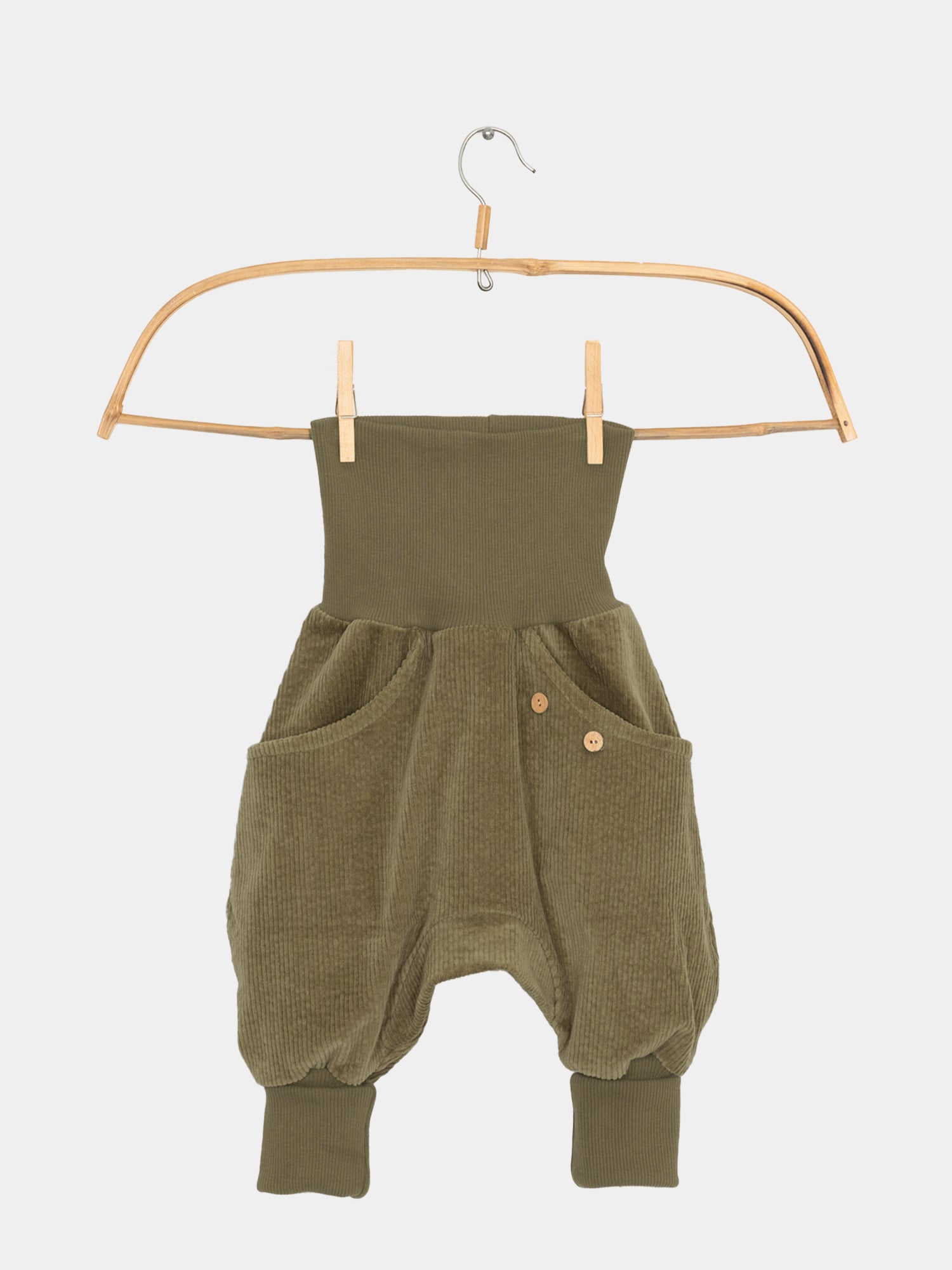 Knickerbocker Breitcord - Kiwi: Eine grüne Cordhose mit Knöpfen und großer Kängurutasche, präsentiert auf einem Holzkleiderbügel. Perfekt für Bewegungsfreiheit und Komfort, ideal für Kinder.