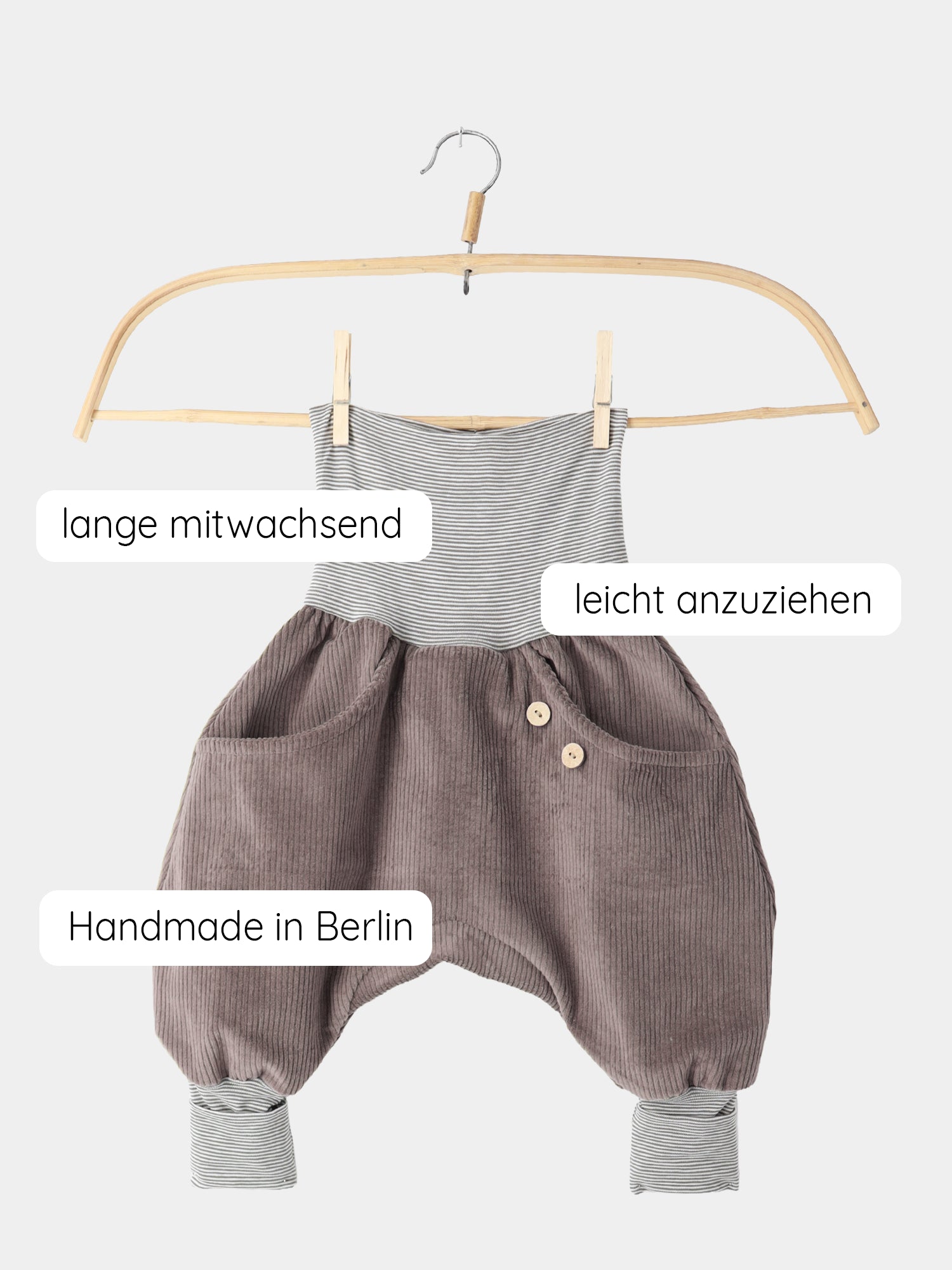 Knickerbocker Breitcord mit Ringelbündchen - Praline: Baby-Romper aus graubraunem Cord, mit gestreiften Bündchen. Hängt auf Holzkleiderbügel. Mit deutschen Callouts: lange mitwachsend, leicht anzuziehen, Handmade in Berlin.