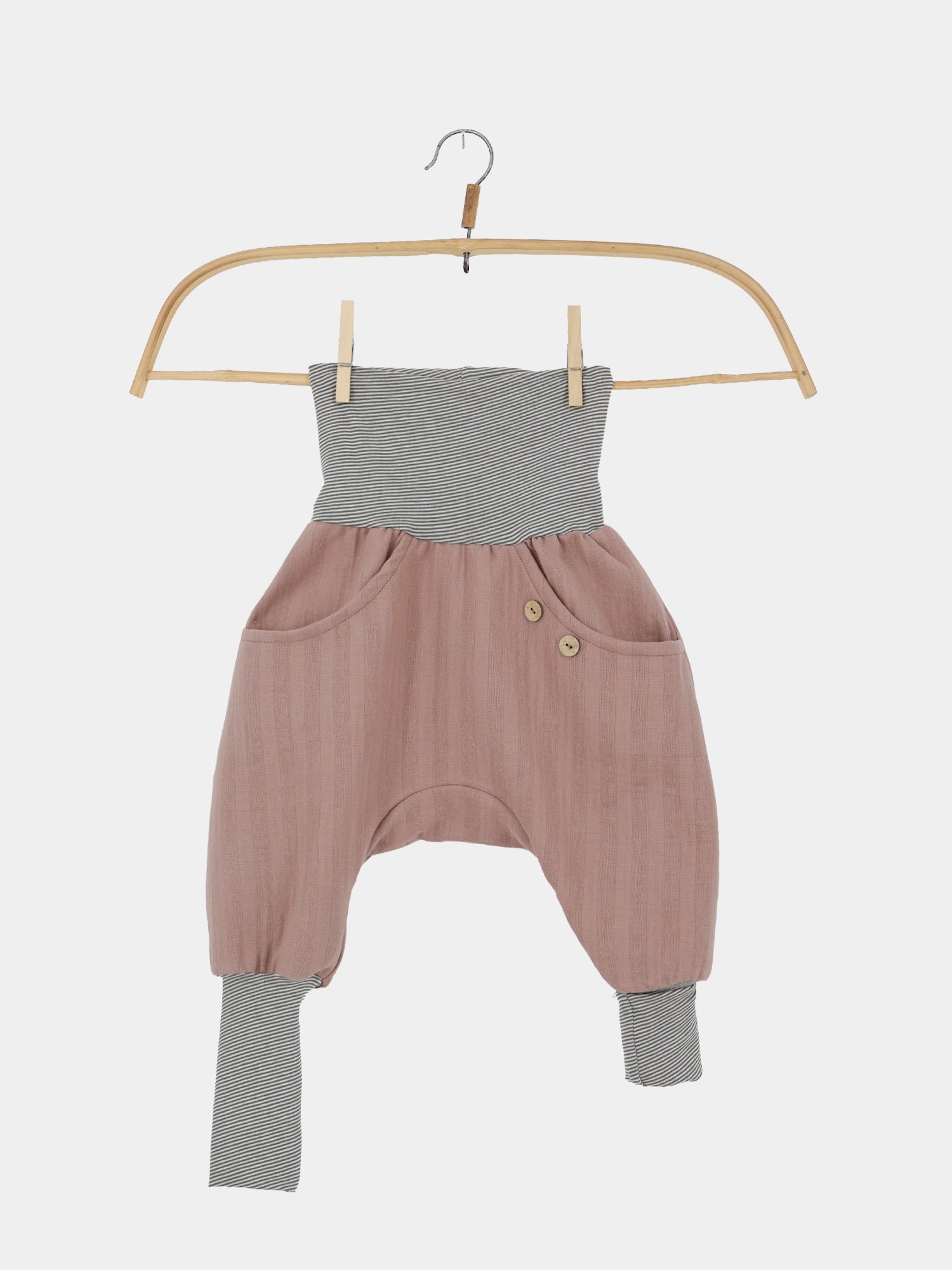 Knickerbocker Musselin aus 100% Bio-Baumwolle - Puder: Kinderharemshose mit zwei Fronttaschen, Holzknöpfen, breitem umklappbarem Bund und Knöchelbündchen aus gestreiftem Strick, hängend an einem Holzkleiderbügel.