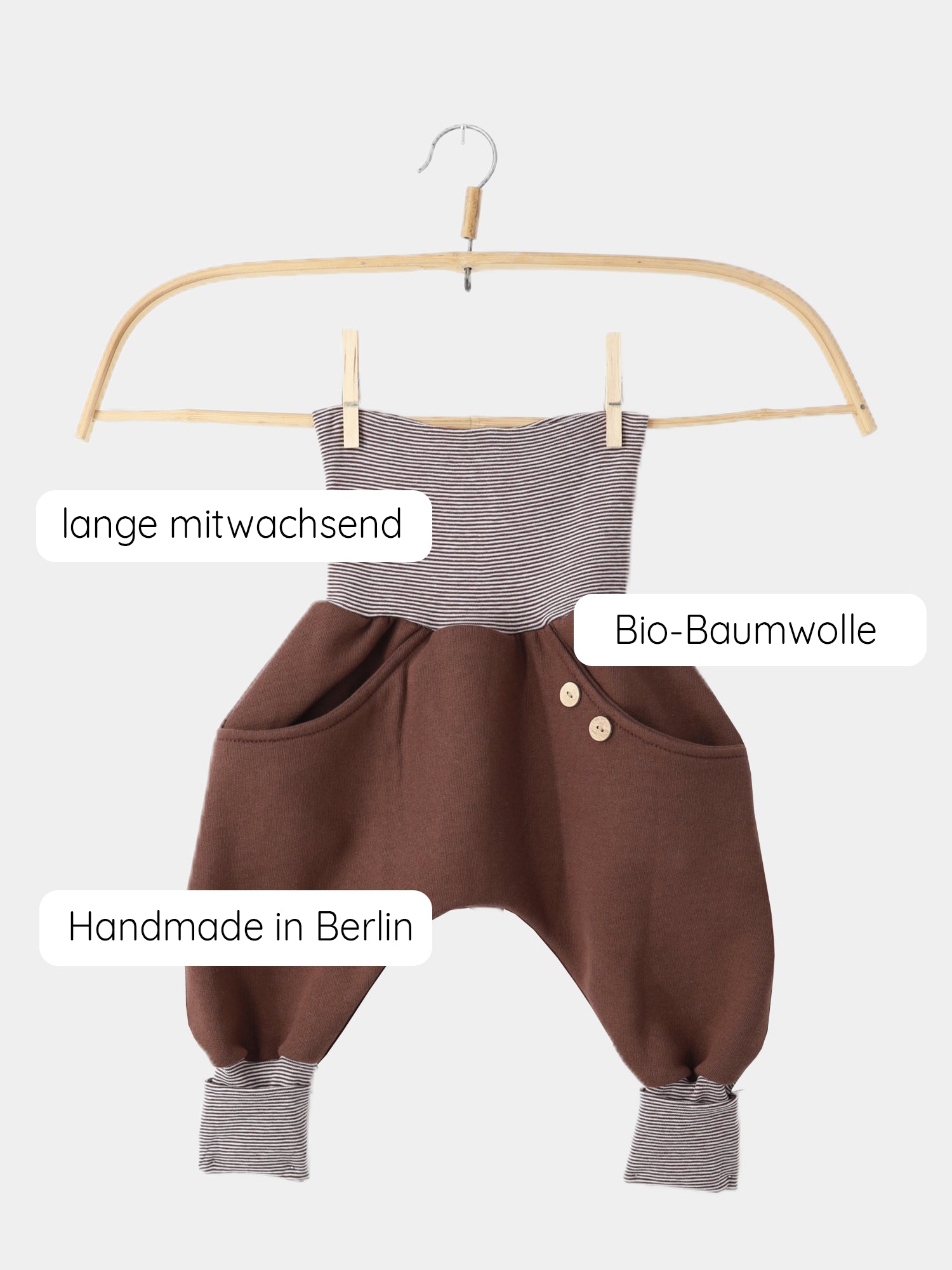 Knickerbocker Bio-Sweat mit Ringelbündchen - Schoko auf Holzbügel. Schokoladenbrauner Bio-Baumwolle-Stoff mit braun-creme Ringelbündchen. Zwei Holzknöpfe an einer Tasche. Handgemacht in Berlin, wächst mit.
