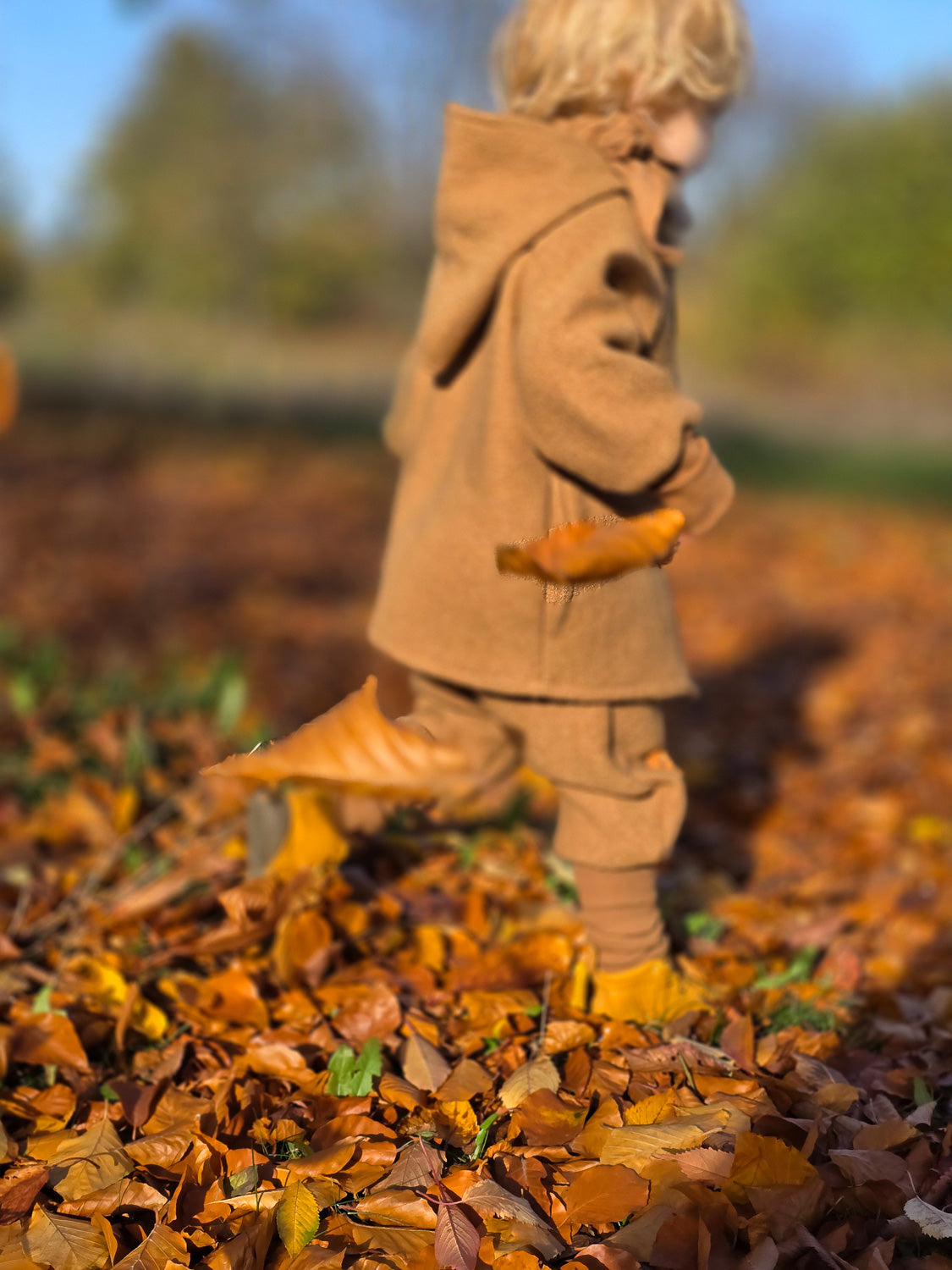 Knickerbocker Wollwalk - Kamel: Ein Kind in einer Wollwalk-Hose mit Kängurutaschen spielt im Herbstlaub. Perfekt für kaltes Wetter, hält trocken und warm. Unisex-Design, ideal für Herbst bis Frühling. nachhaltige Kinderkleidung aus Wollwalk