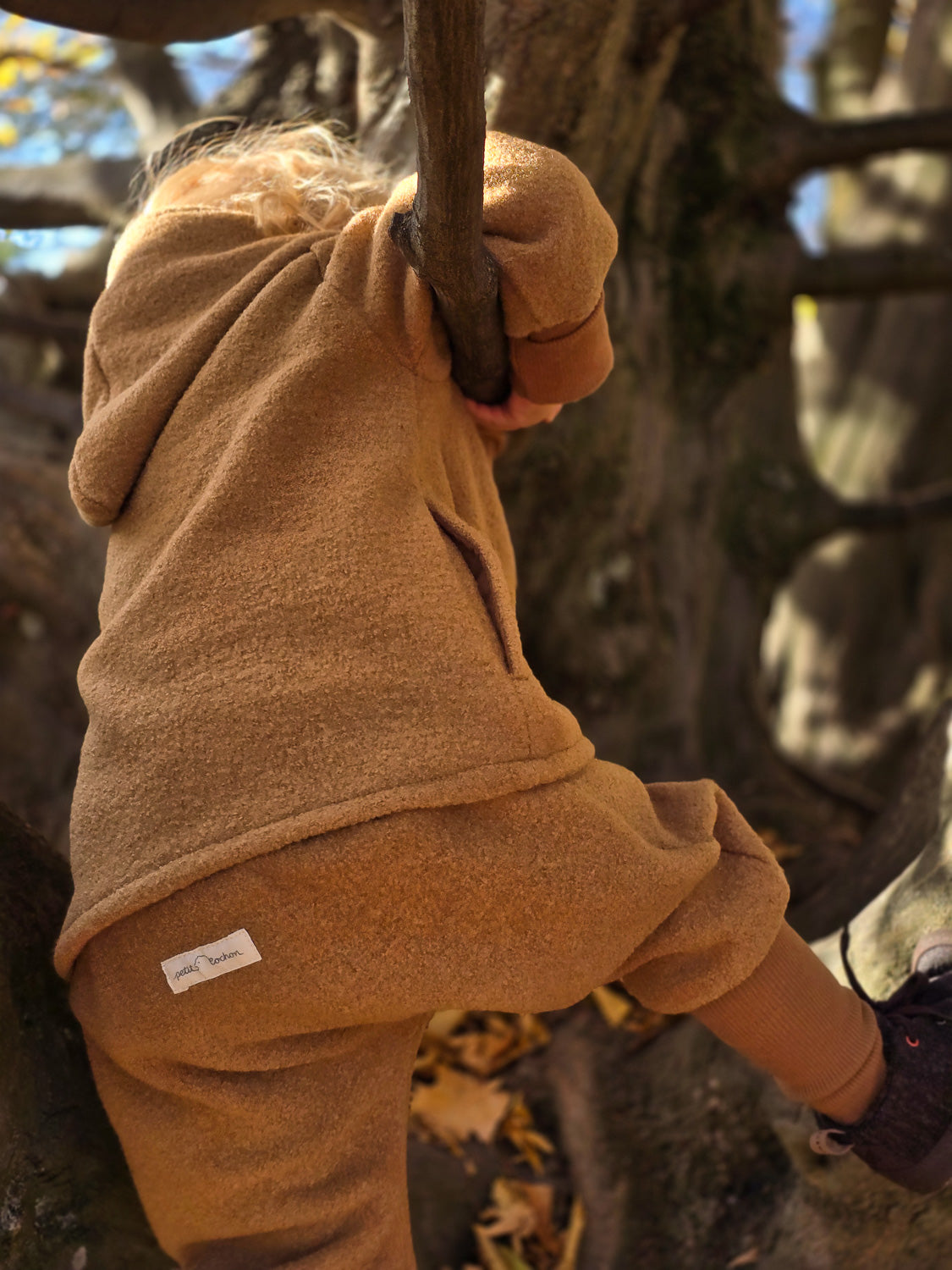 Kind klettert auf Baum in Knickerbocker Wollwalk - Kamel, robust für kaltes Wetter, mit Kängurutaschen, ideal für draußen, unisex Design, handgefertigt in Berlin. nachhaltige Kinderkleidung aus Wollwalk