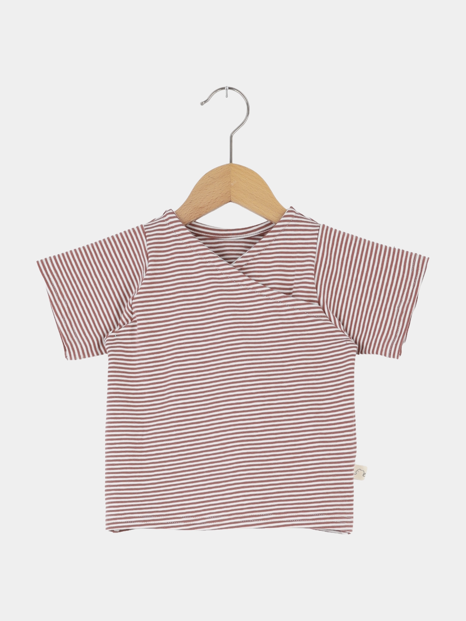 Kurzes Wickelshirt Baumwolle - Ringel Ziegel: Kinder T-Shirt aus weichem, gestreiftem Stoff mit Wickelausschnitt, auf Holzbügel vor weißem Hintergrund. Perfekt für sommerliche Outfits, handgemacht in Berlin.