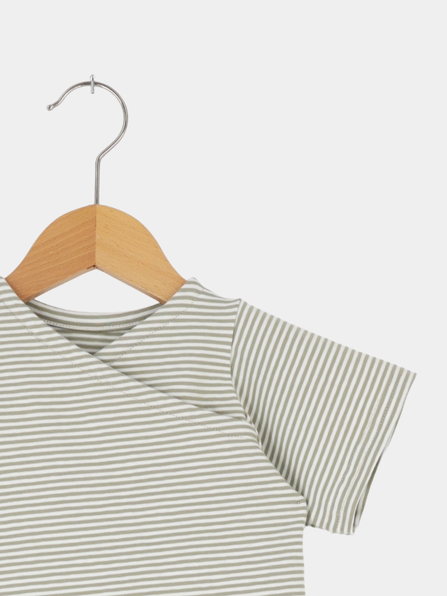 Kurzes Wickelshirt Baumwolle - Ringel Salbei: Ein Oberteil mit kurzen Ärmeln und Wickelausschnitt, aus dünn gestreiftem, sagefarbenem Stoff, hängend an einem Holzkleiderbügel.