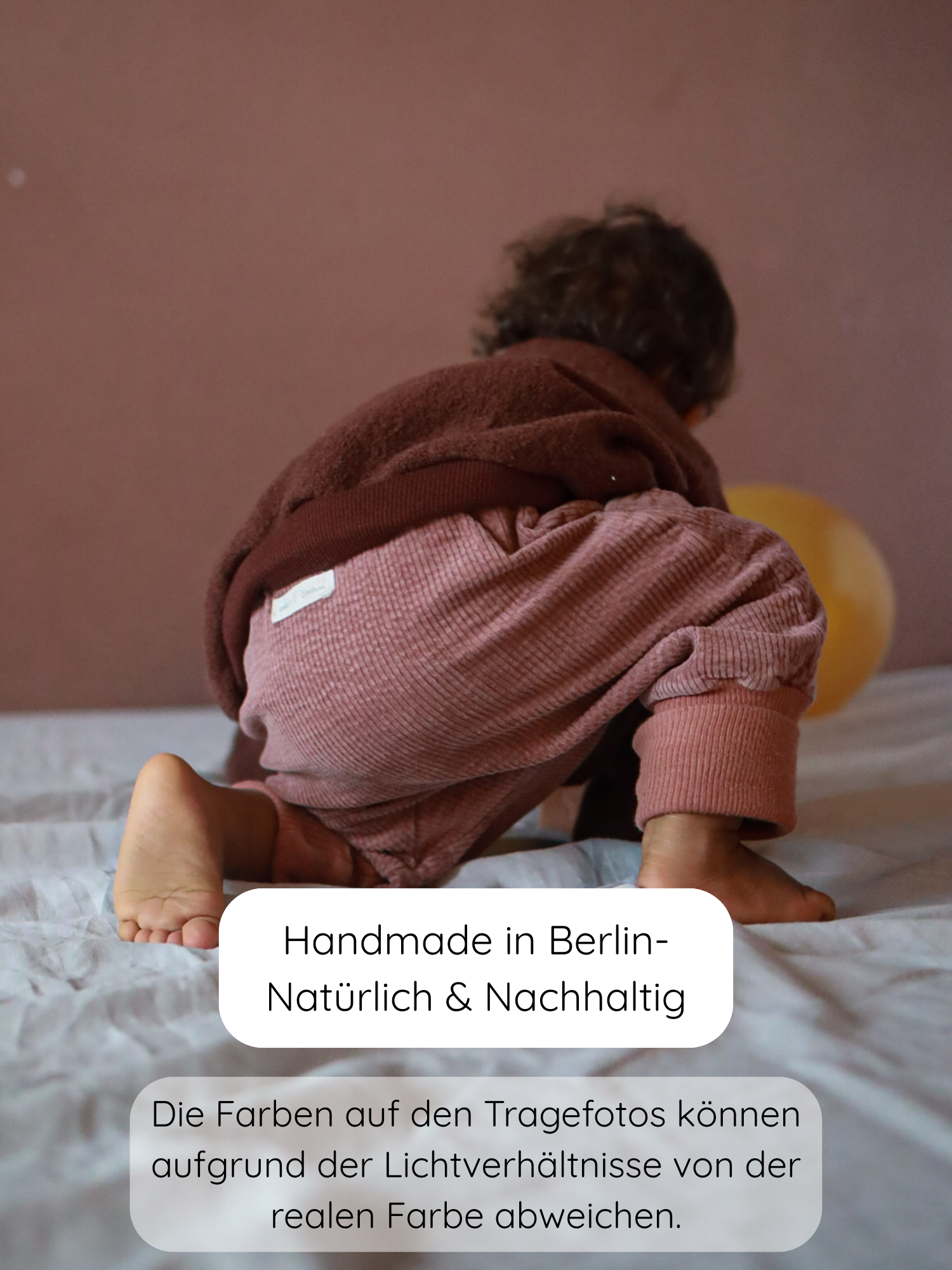 Kind krabbelt auf einem Bett in ribbigen, Rosenholz-Knickerbocker-Hosen und braunem Oberteil. Der Fokus liegt auf der Knickerbocker Breitcord Stretch - Rosenholz, handgefertigt in Berlin.