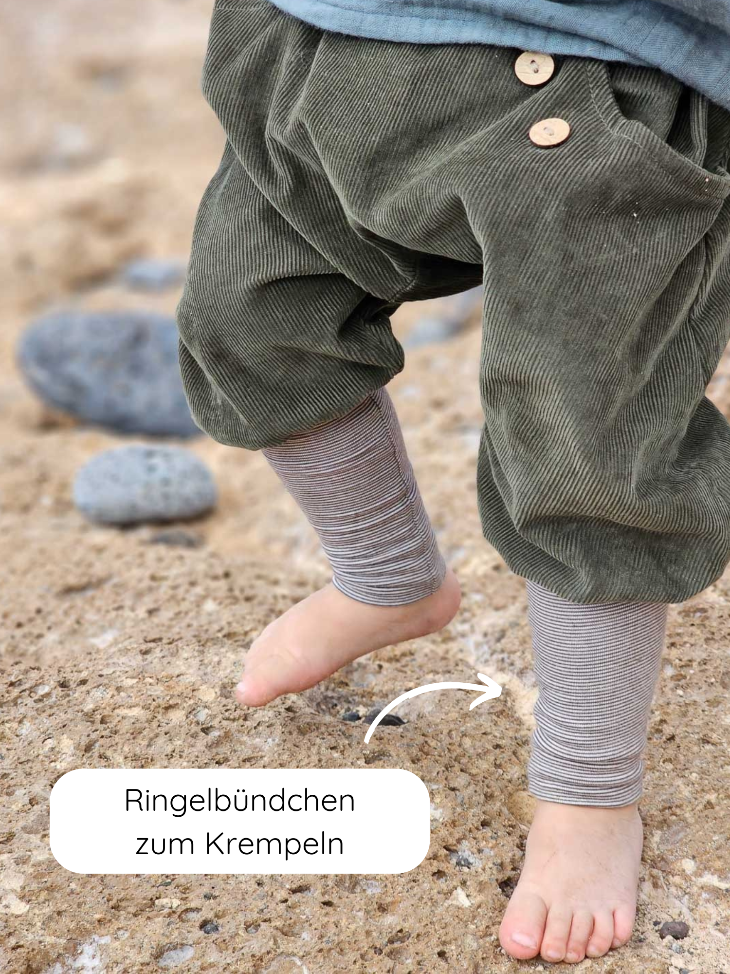 Ein kleines Kind trägt Knickerbocker Feincord Ringel - Avocado mit gestreiften Bündchen und Holzknöpfen, steht barfuß auf Sand; ideal für aktive Kinder, handgemacht in Berlin.
