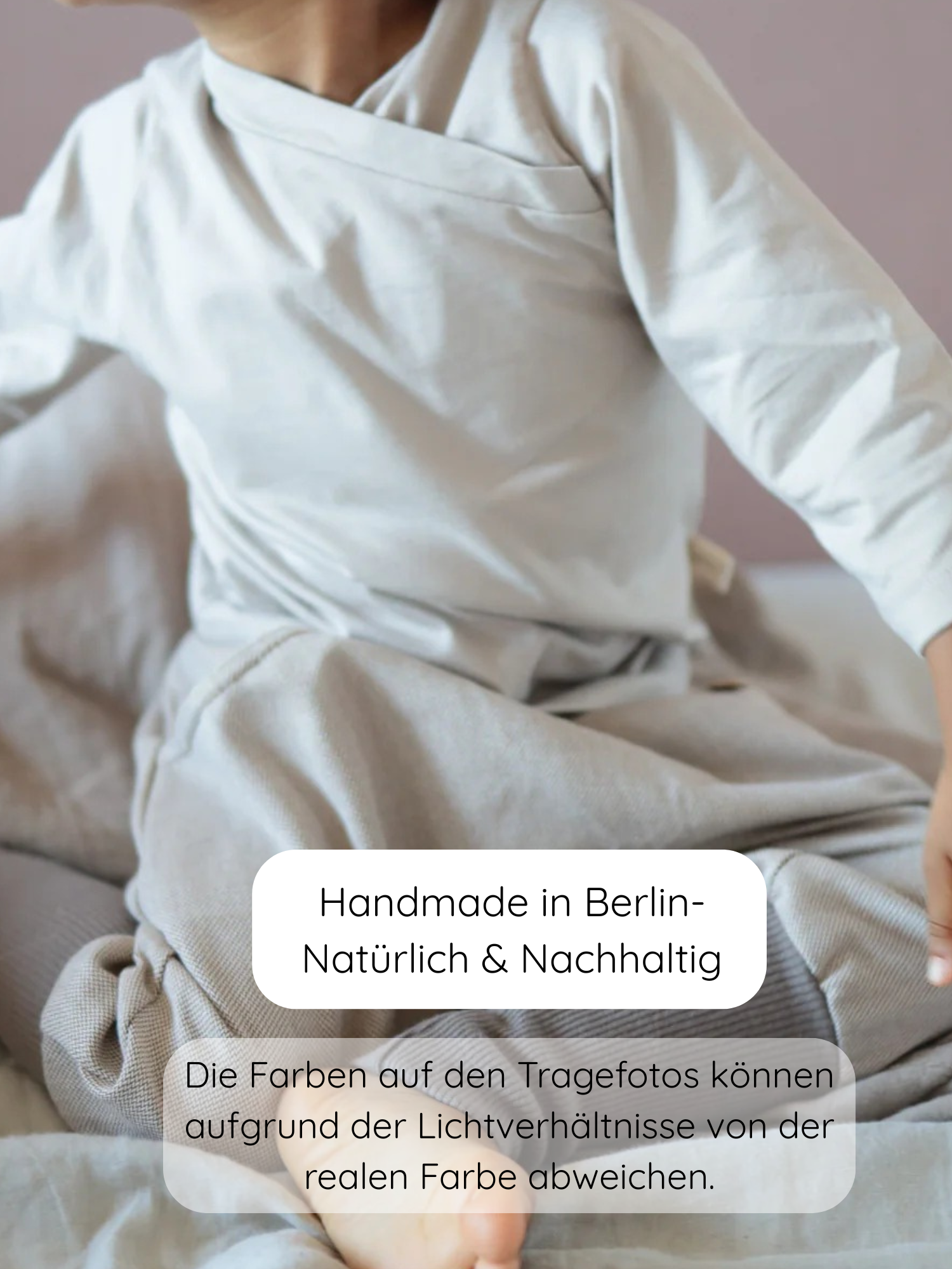 Kind in neutralem, langärmligem Oberteil und passender Hose, „Knickerbocker Feincord Ringel - Sand“, zeigt handgemachte, nachhaltige Kinderkleidung aus Berlin. Text warnt vor möglichen Farbabweichungen durch Lichtverhältnisse.