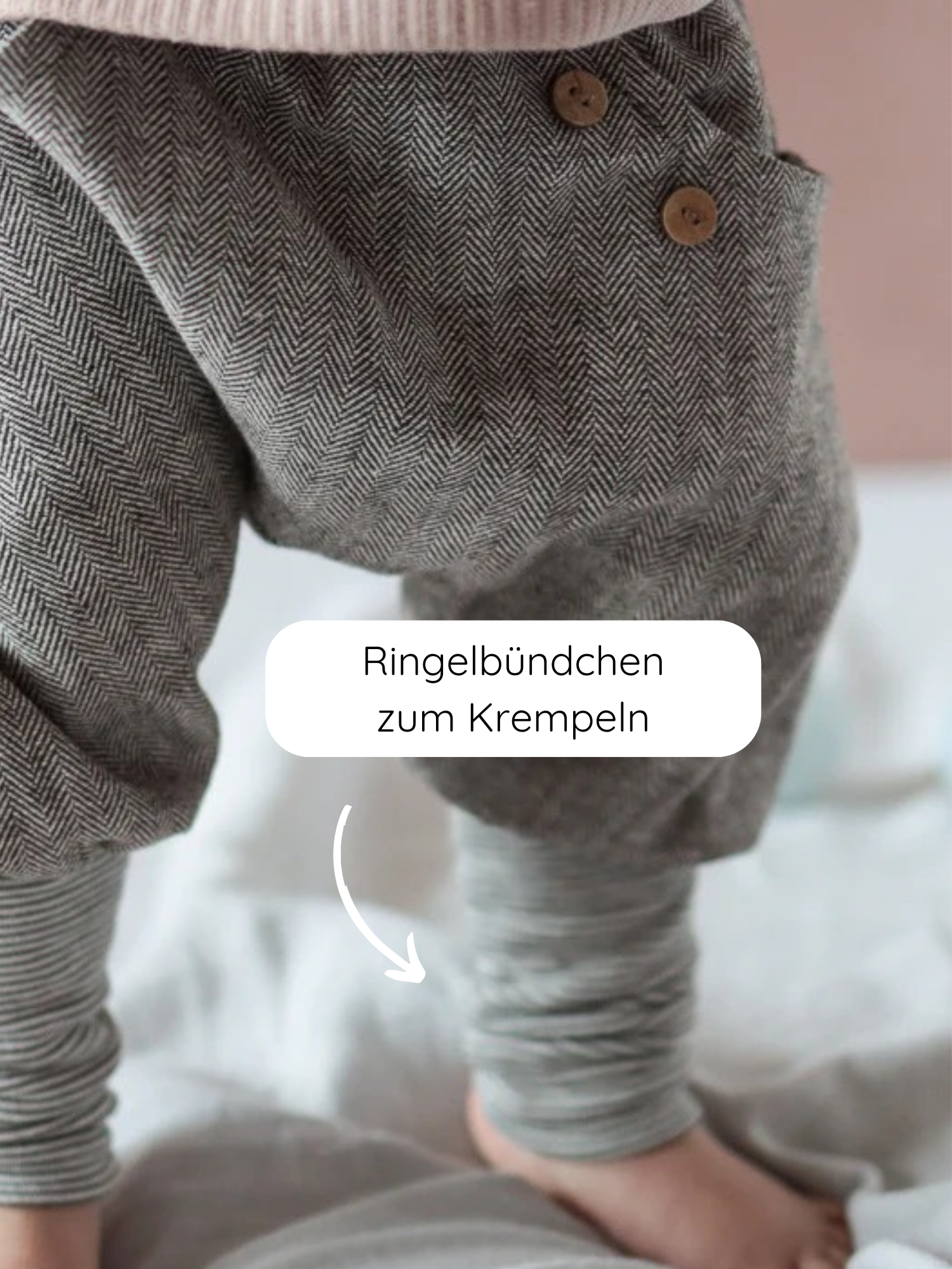 Knickerbocker Fischgrat: Nahaufnahme von grauen Fischgrathosen für Kleinkinder mit zwei Holzknöpfen an der Taille und umkrempelbaren, gestreiften Bündchen an den Knöcheln.