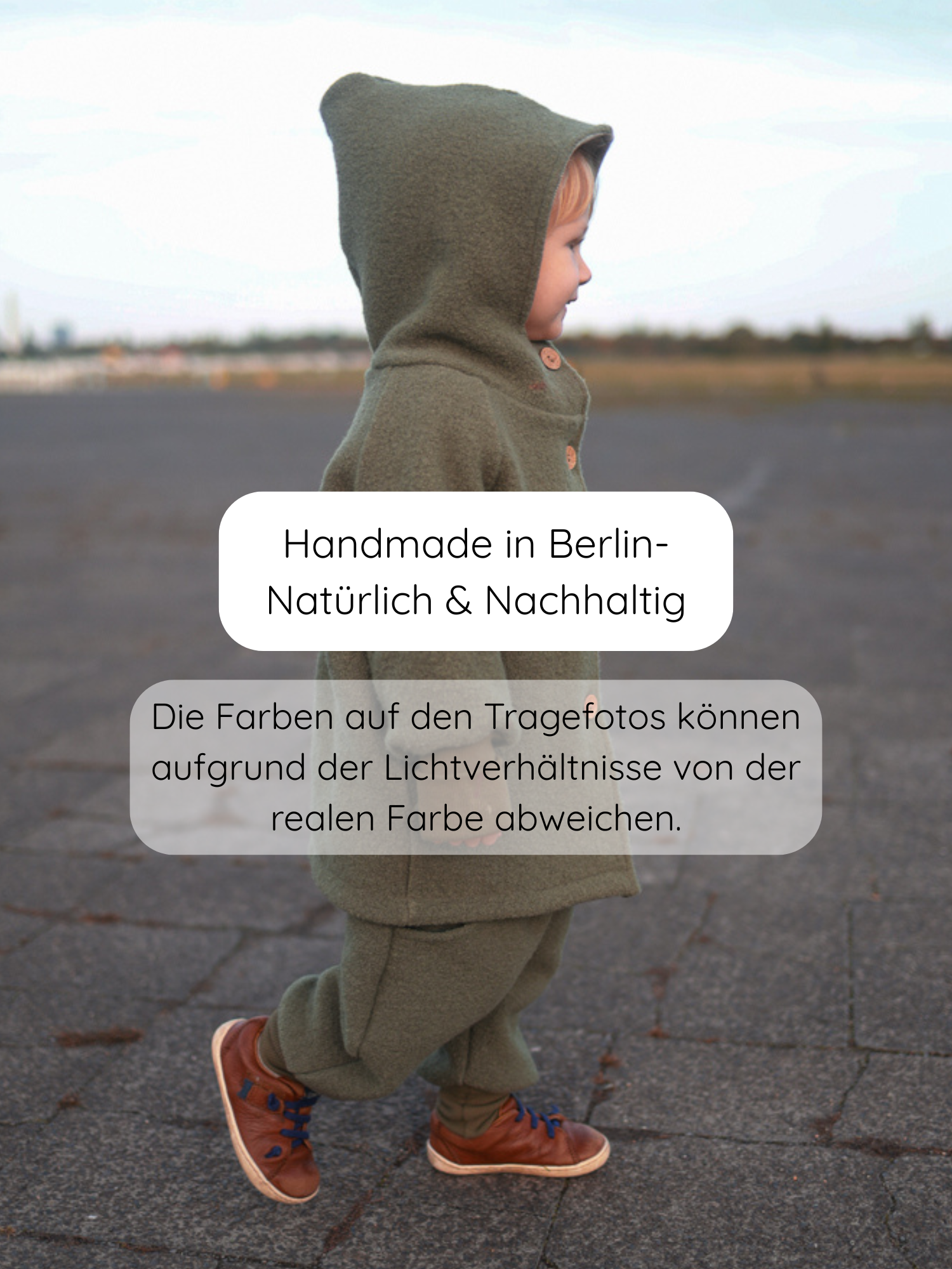 Kind im Profil auf Asphalt trägt Knickerbocker Wollwalk - Pistazie: olivgrüne Kapuzenjacke, lockere Hose mit breiten Bündchen, braune Ledersneaker. Text: Handmade in Berlin – Natürlich & Nachhaltig.
