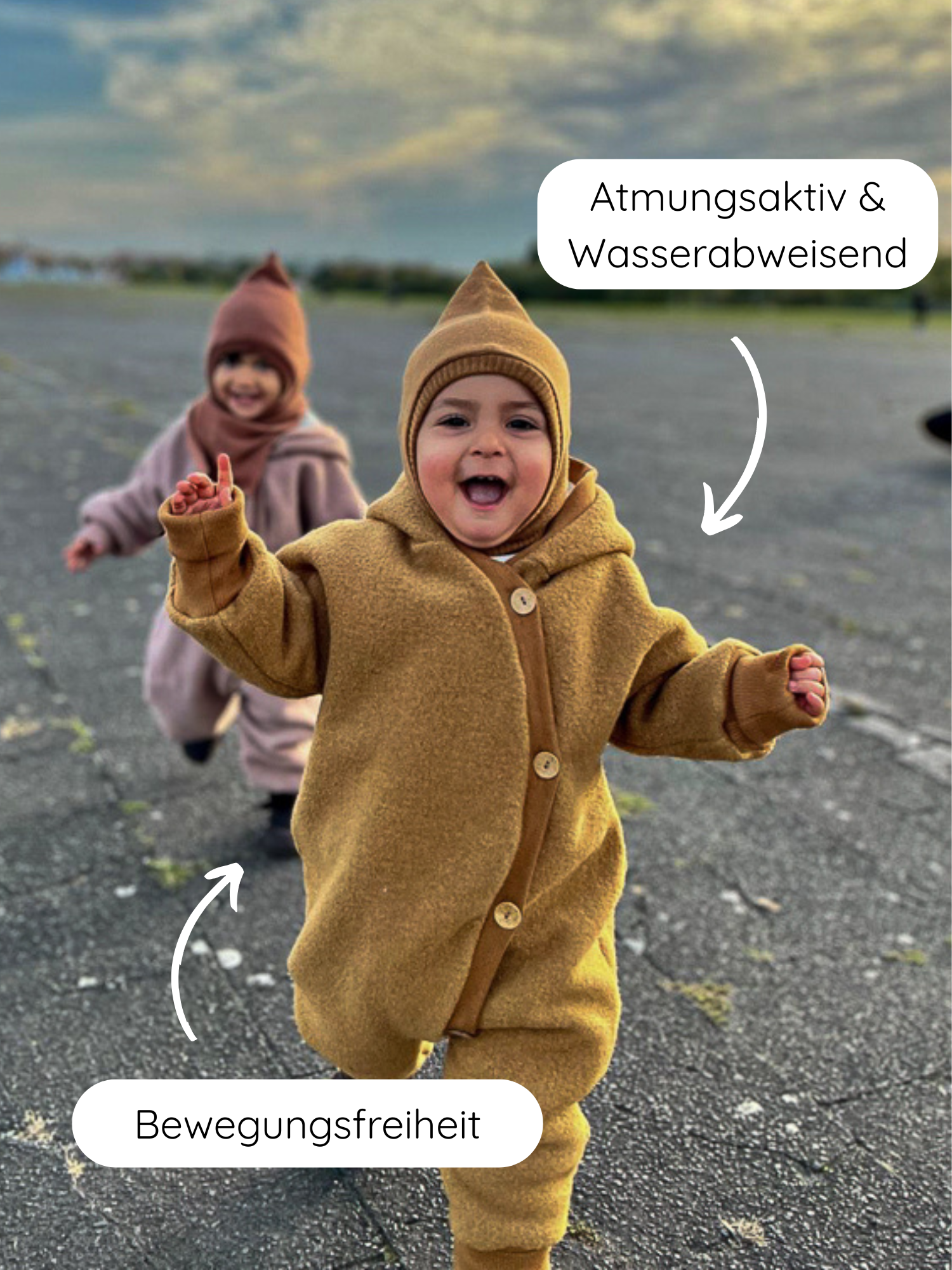 Zwei Kleinkinder in Kuschelanzug Wollwalk - Honig rennen auf einer alten Startbahn. Der Anzug bietet Bewegungsfreiheit, ist atmungsaktiv und wasserabweisend, ideal für Frühling bis Winter.