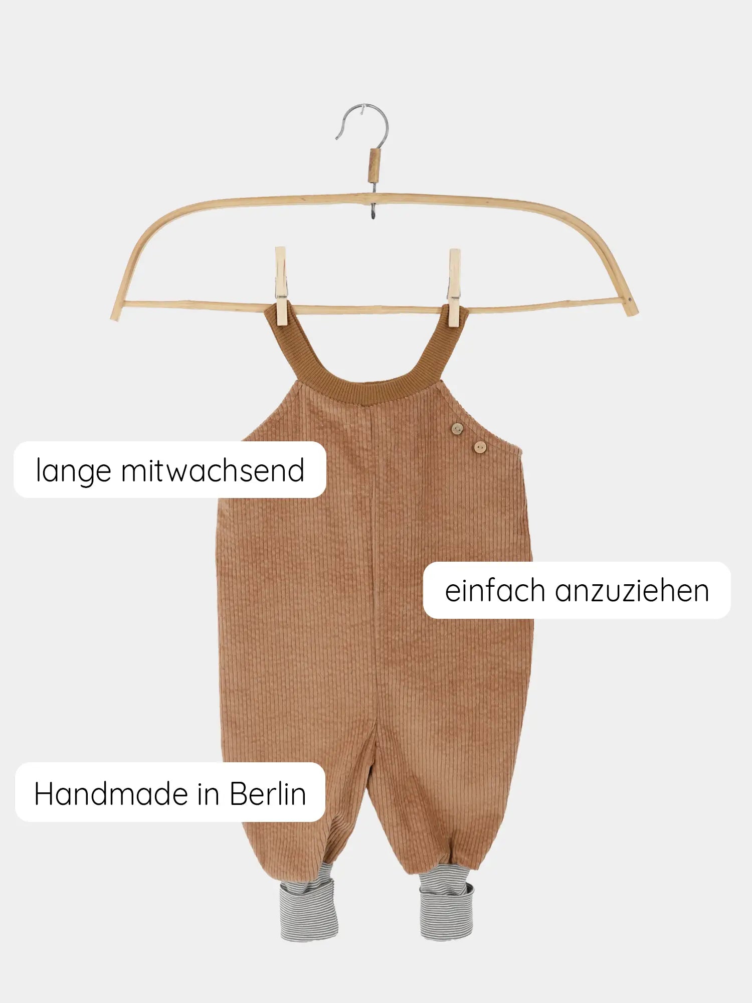 Schlupflatzhose Breitcord - Weizen: Brauner Cord-Romper mit verstellbaren Schulterträgern und gestreiften Bündchen, auf Holzkleiderbügel. Handgemacht in Berlin, einfach anzuziehen, mitwachsend, ideal für Stoffwindeln.