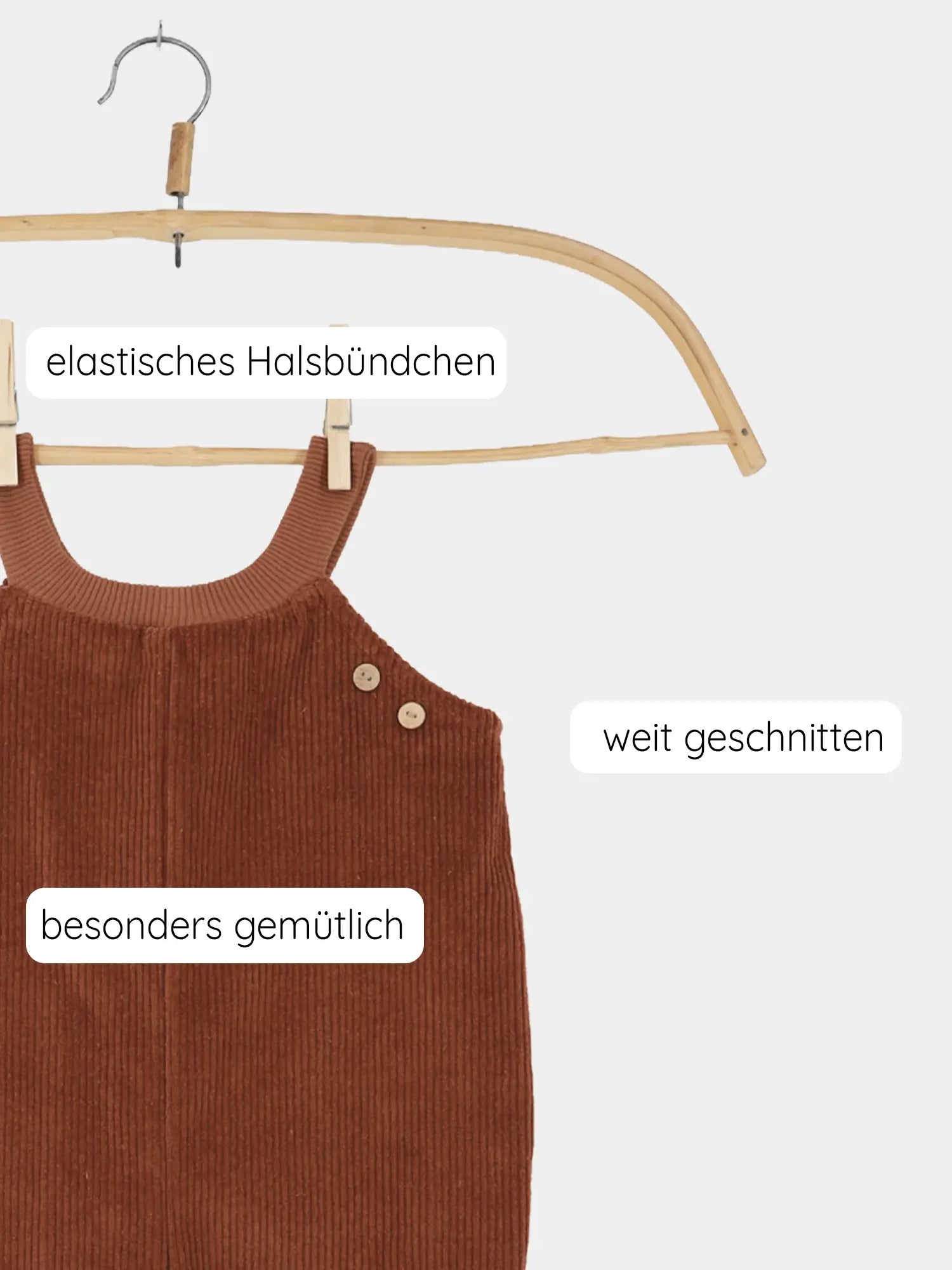 Schlupflatzhose Breitcord - Rost: Kinder-Romper aus braunem, geripptem Stoff, hängt an Holzkleiderbügel mit zwei Holzknöpfen an einem Schulterträger. Text betont elastischen Halsbund, weiten Schnitt, Gemütlichkeit.