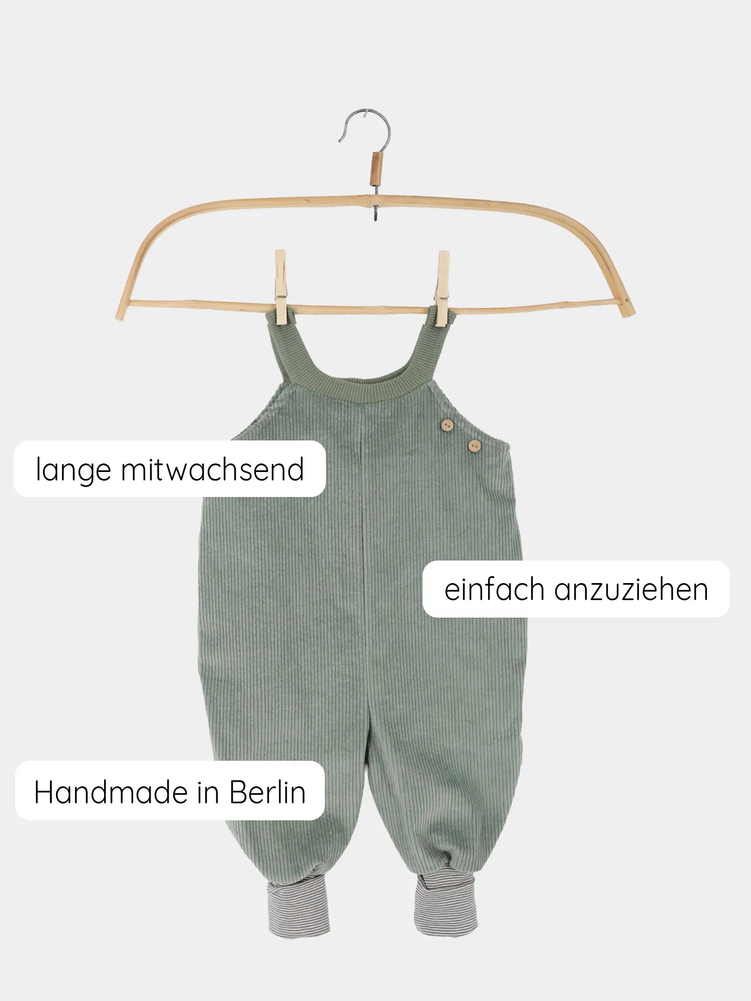 Schlupflatzhose Breitcord - Aqua: Ein sage-grüner, gerippter Babyromper mit Holzknöpfen an den Trägern, gestreiften Bündchen und den Merkmalen „lange mitwachsend“, „einfach anzuziehen“, „Handmade in Berlin“.