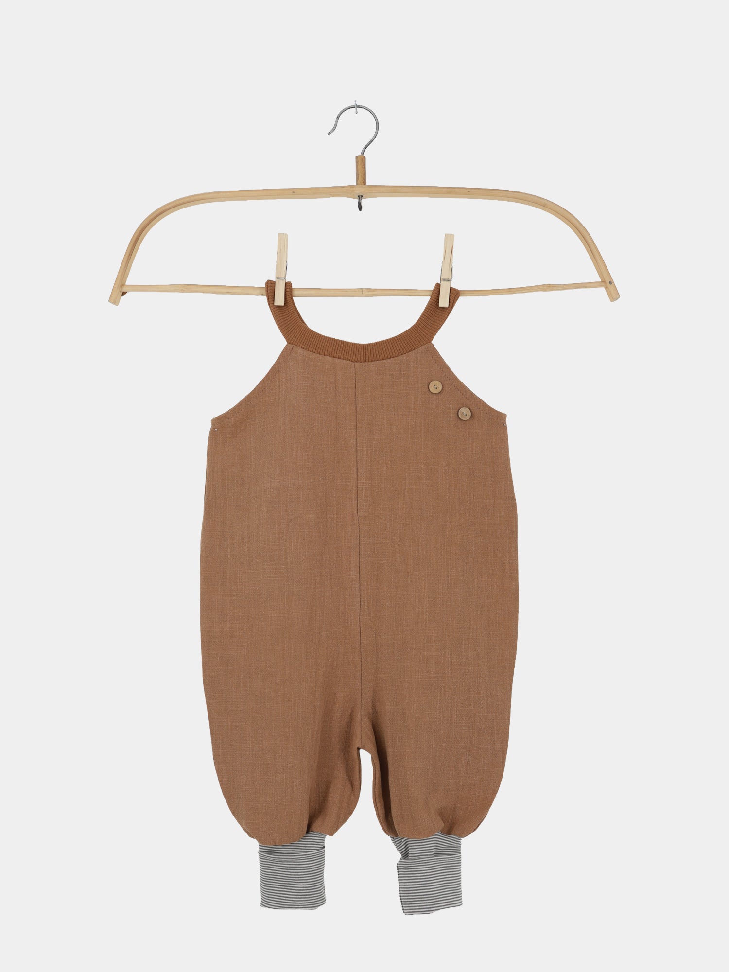 Schlupflatzhose Leinen - Weizen: Ein brauner Leinenromper für Kleinkinder mit Halterneck, Holzknöpfen und grauen gestreiften Bündchen an den Beinen, hängend an einem Holzbügel.
