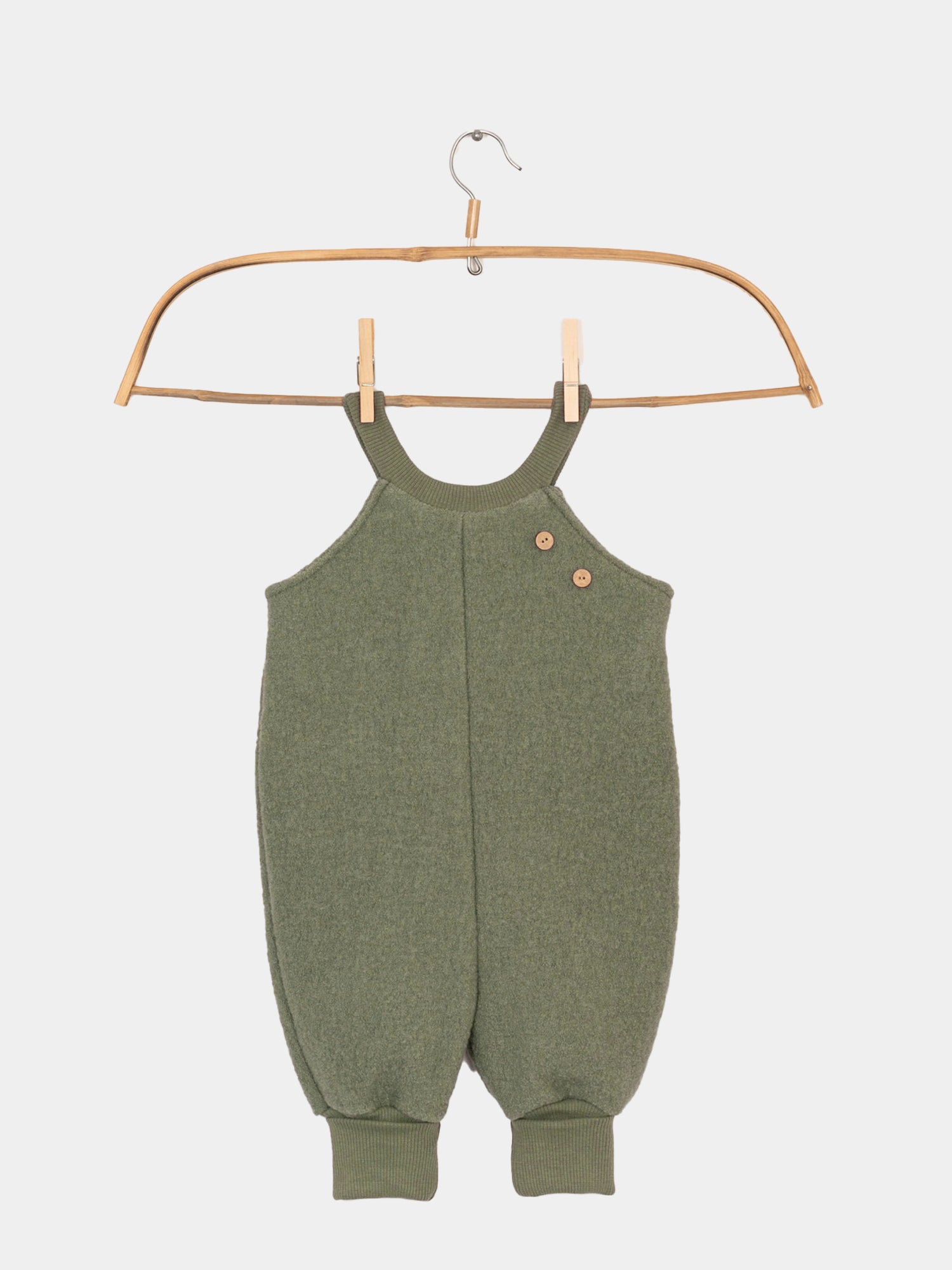 Schlupflatzhose Wollwalk- Pistazie von PETIT COCHON, ein grüner Babystrampler aus 100% Schurwolle, ideal für Kälte- und Nässeschutz, auf einem Holzbügel dargestellt.