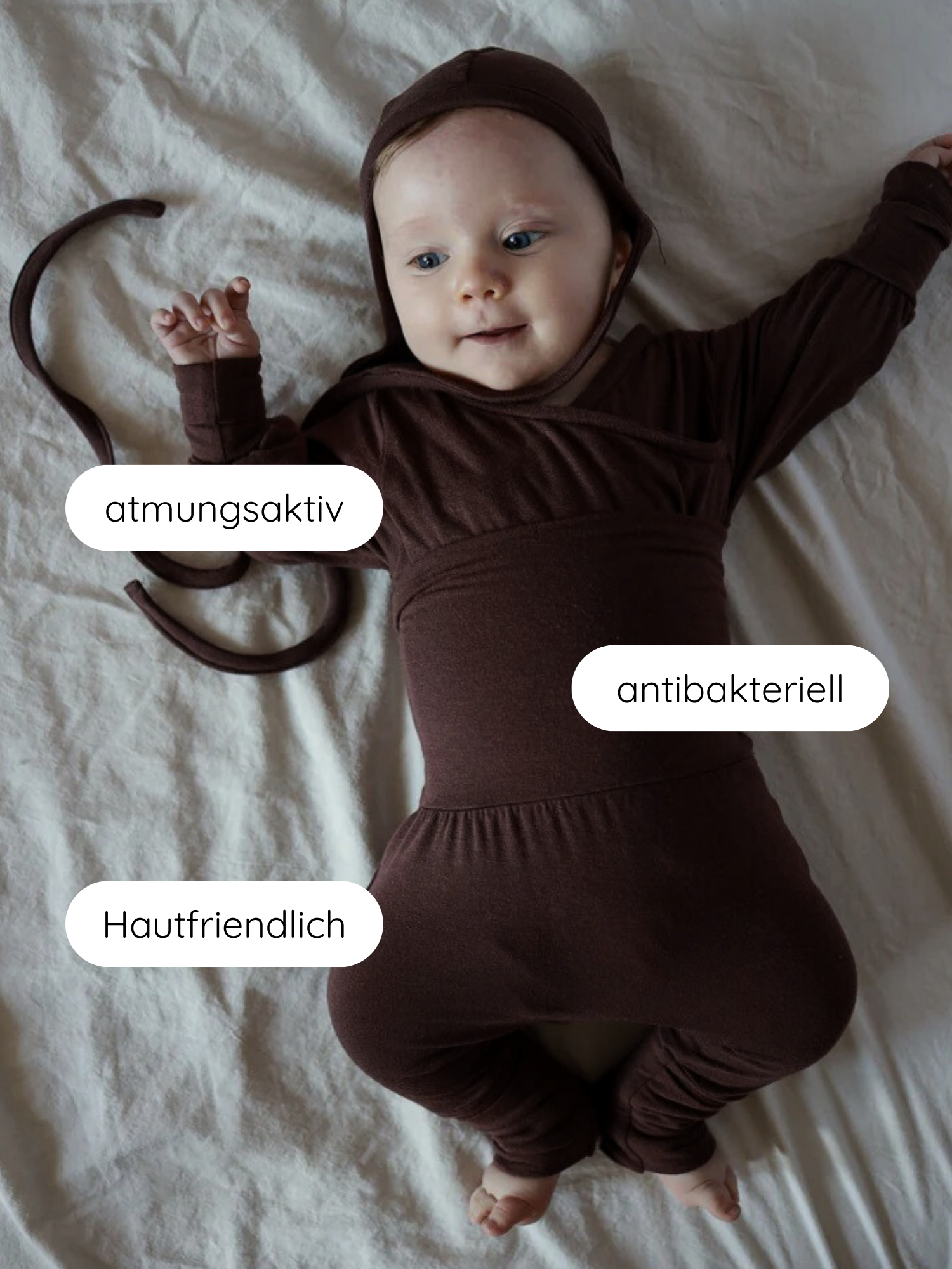 Ein Baby liegt in einem Loopbody Bambusviskose - Zartbitter, einem braunen, mitwachsenden, atmungsaktiven Einteiler mit Kapuze, ausgezeichnet für Hautfreundlichkeit und Antibakterialität, ideal für einfaches Wickeln.
