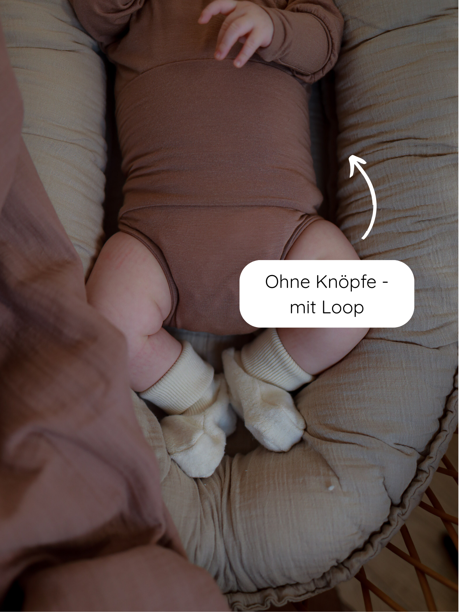Baby in einem Loopbody Kaschmir-Mix - Puder auf gepolstertem Babykissen. Der langärmelige Body ohne Knöpfe ist bequem, mitwachsend und hat einen Loop für zusätzlichen Komfort und Wärme.
