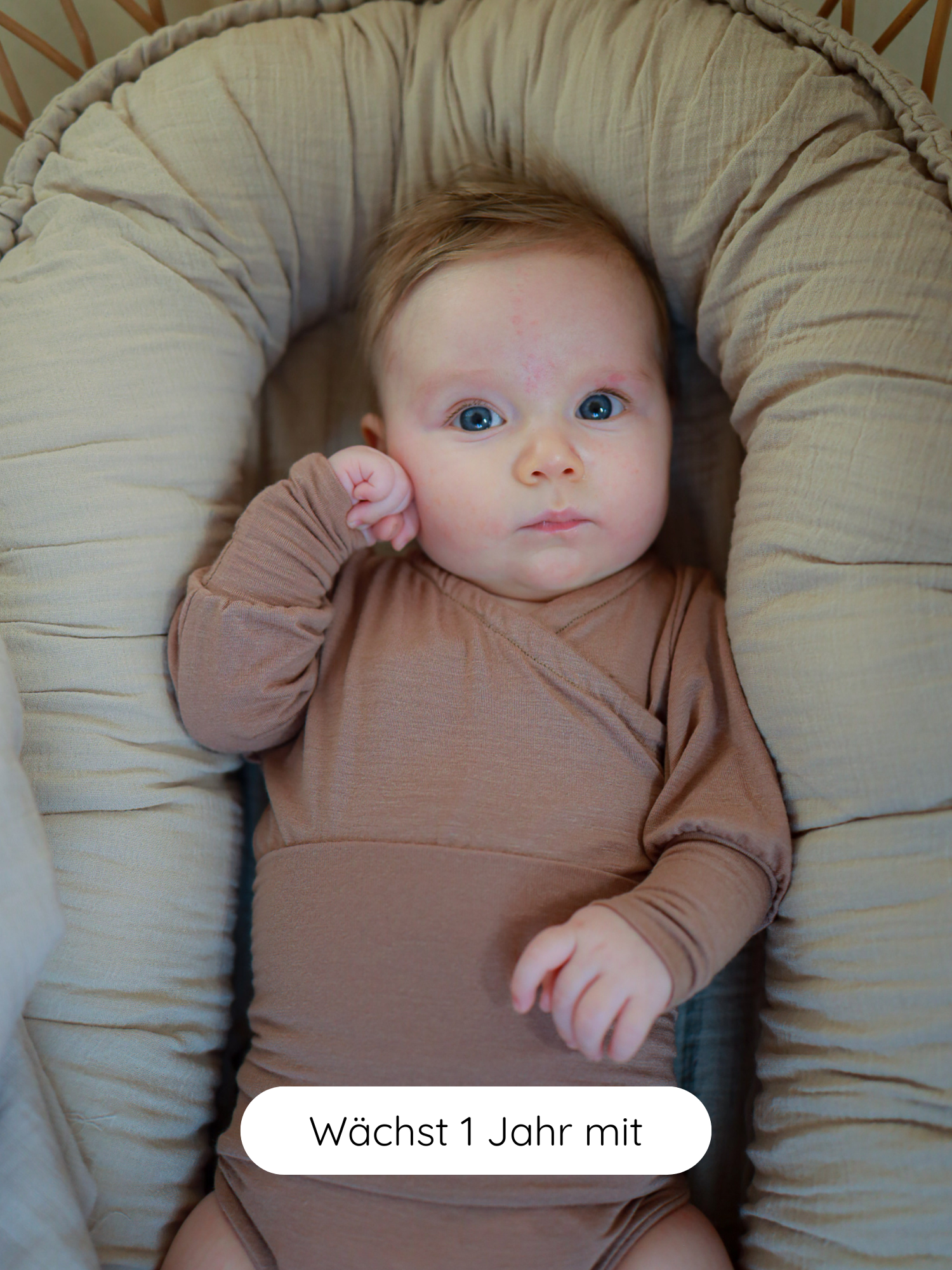 Ein Baby liegt in einem gepolsterten Nest, trägt einen Loopbody Kaschmir-Mix - Puder. Der anschmiegsame, langärmlige Body ist weich und wächst mit, ideal für Komfort und Wärme.