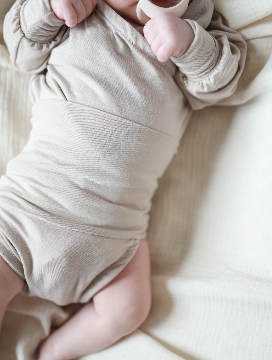 Baby liegt auf Rücken. Trägt Loopbody Kaschmir-Mix - Sand, langärmlig, ohne Knöpfe, mit Loop für einfachen Wechsel und extra Wärme, aus weichem Kaschmir-Mix. Erstausstattung Baby und Baby Geschenk zur Geburt.