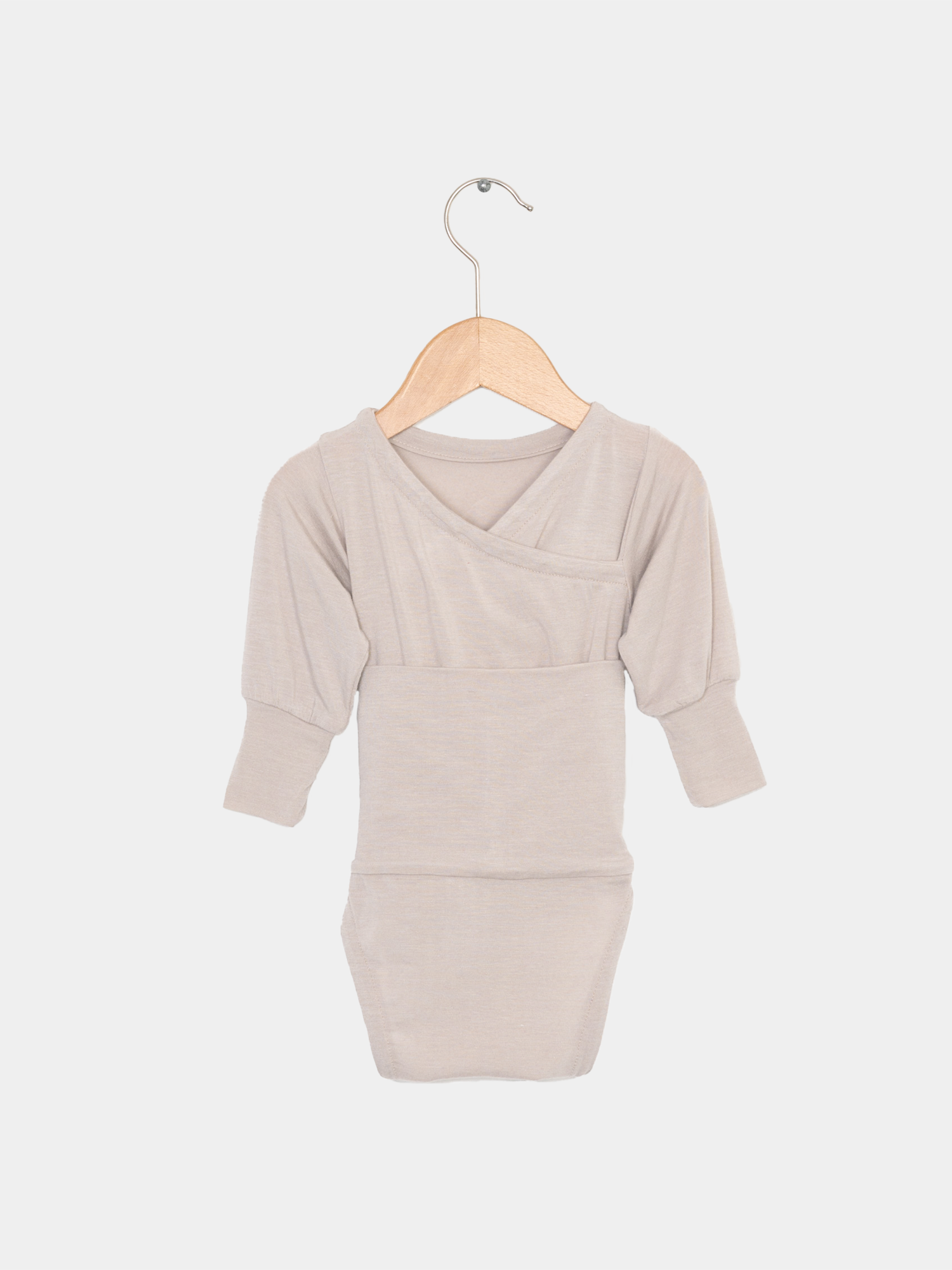 Loopbody Kaschmir-Mix - Sand auf einem Holzbügel mit Metallhaken. Beige Langarmbody ohne Knöpfe, aus Kaschmir-Mix, weich und anschmiegsam, ideal für Babys, das mitwächst und preisgekrönt ist.