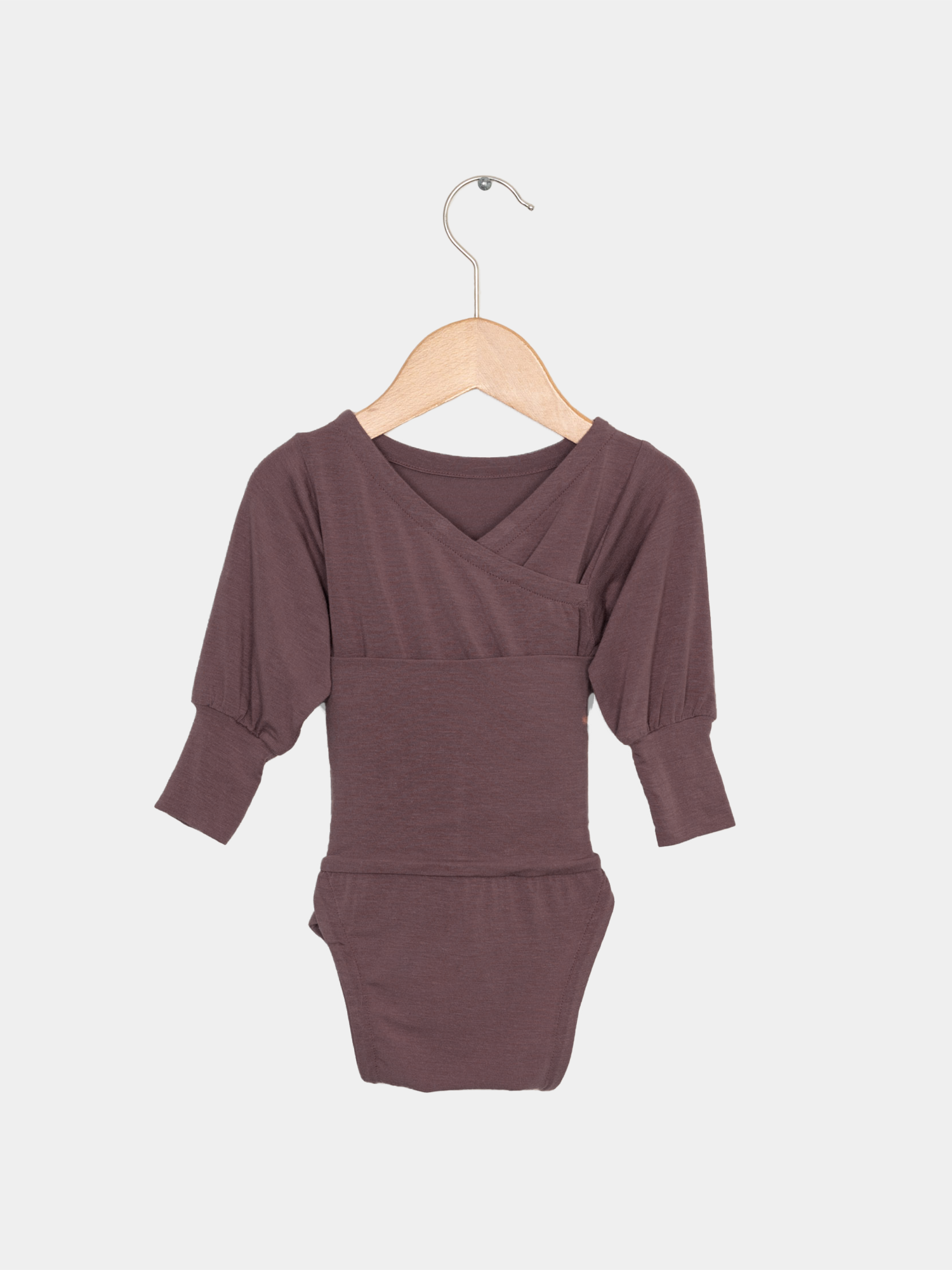 Ein lilafarbener Loopbody Kaschmir-Mix für Babys, ohne Knöpfe, auf einem Holzaufhänger. Besonders weich, wächst mit, ideal für bequemes An- und Ausziehen.
