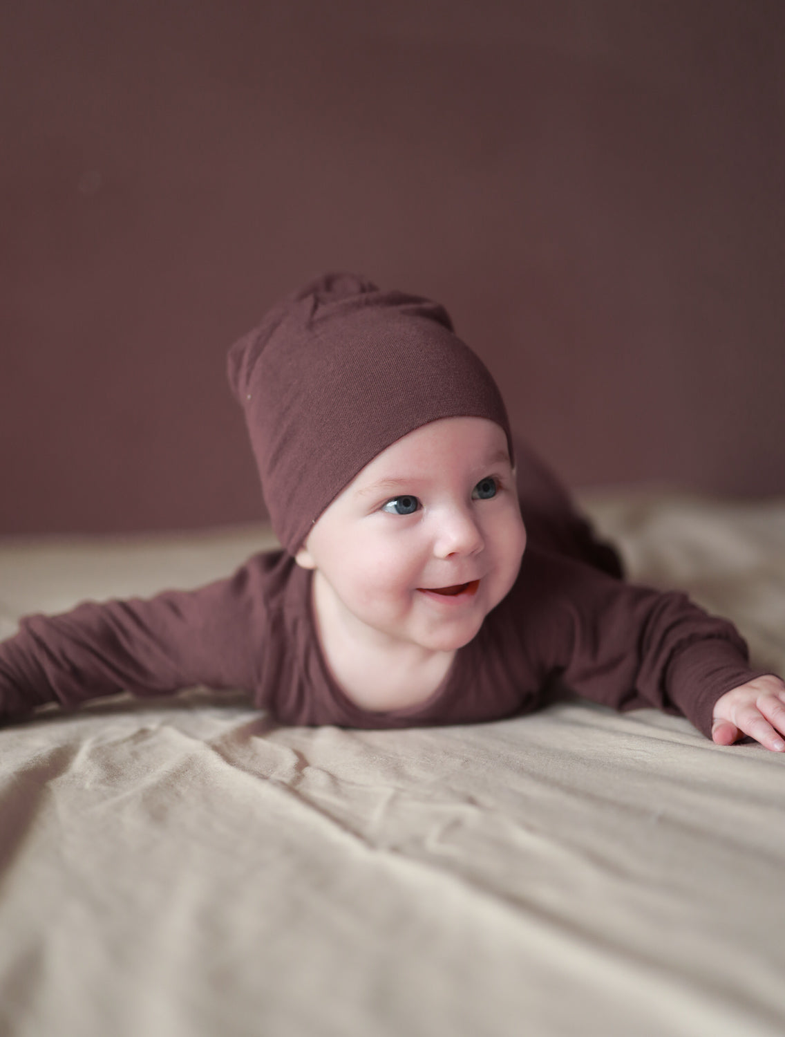 Baby in Kaschmir-Mix Loopbody ohne Knöpfe, liegend auf einem Bett. Der weiche, atmungsaktive Body umschließt den Bauch für einfaches Anziehen. perfekte Baby Geschenke.