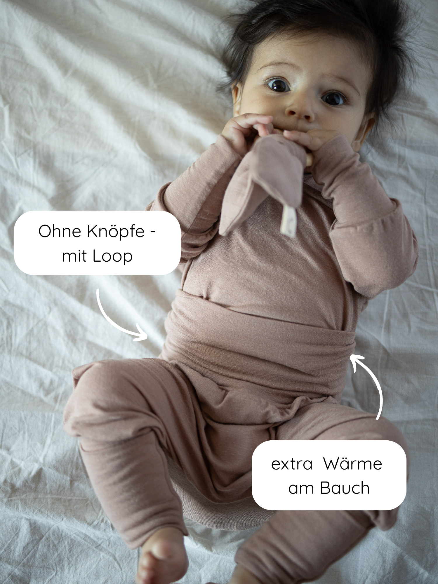 Baby in Loopstrampler Kaschmir-Mix - Puder mit Wickelverschluss und ohne Knöpfe. Zusätzliche Bauchwärme durch Loop-Design. Baby hält ein weiches Spielzeug.