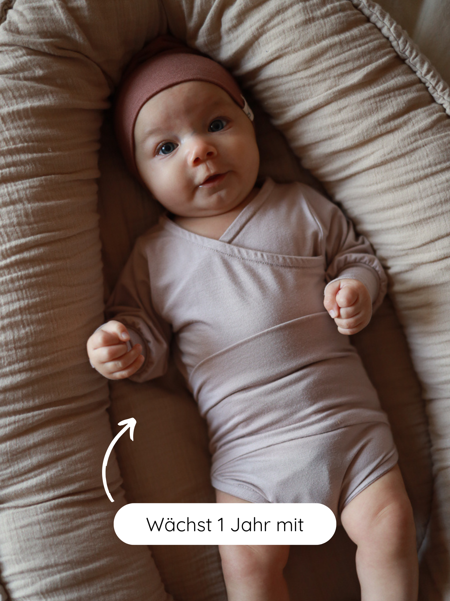 Kleines Baby in einem kuscheligen Babynest, trägt den Loopbody Bambusviskose - Cremepuder, der mitwachsend ist und über ein Jahr passt. Pfeil zeigt auf Polsterung mit „Wächst 1 Jahr mit“-Hinweis.