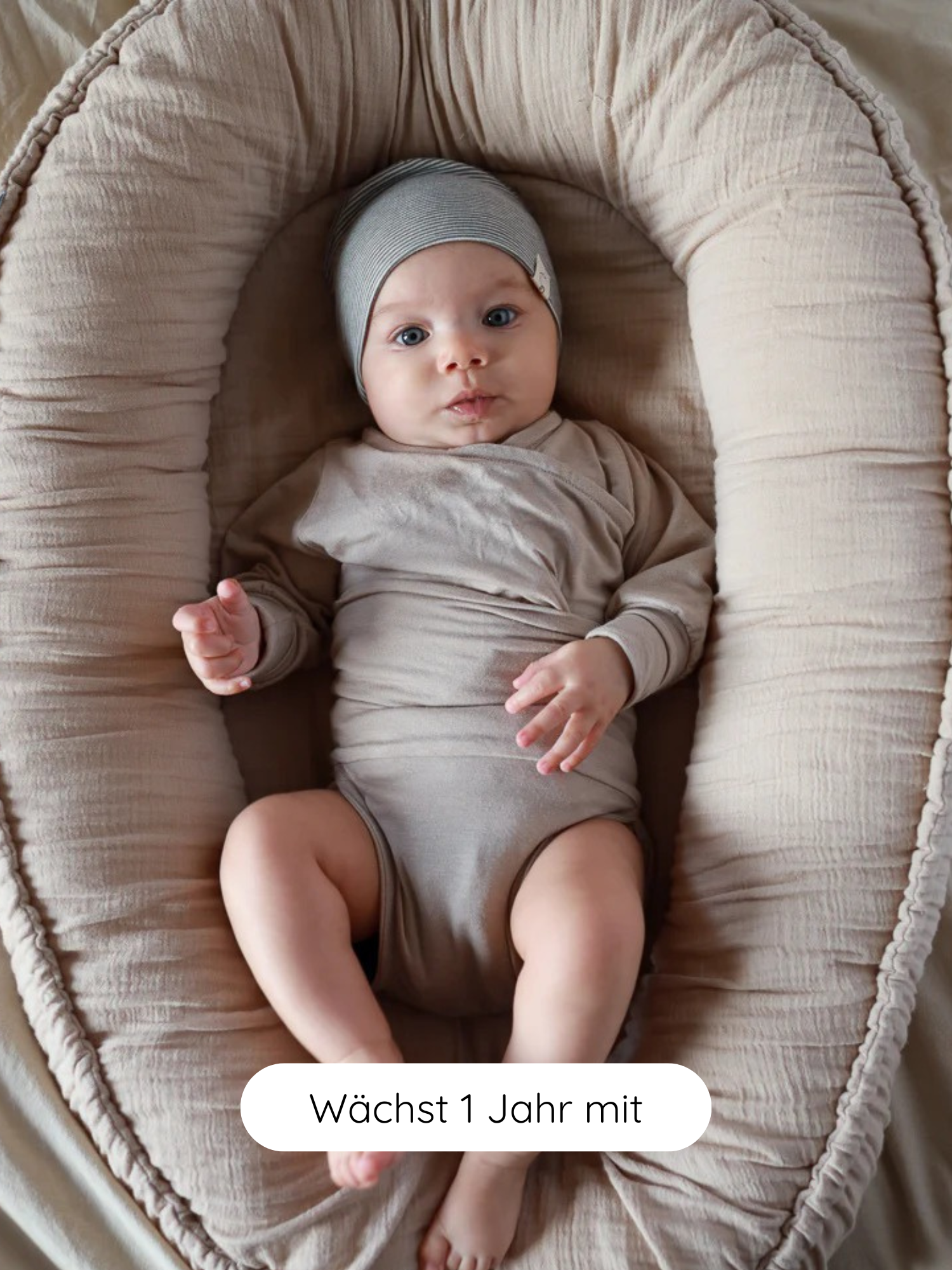 Baby liegt in einem weichen, beigen Nest, trägt einen Loopbody Kaschmir-Mix - Sand. Der Body ist langärmelig, ohne Knöpfe, aus Kaschmir-Mix, mitwachsend bis zu einem Jahr.