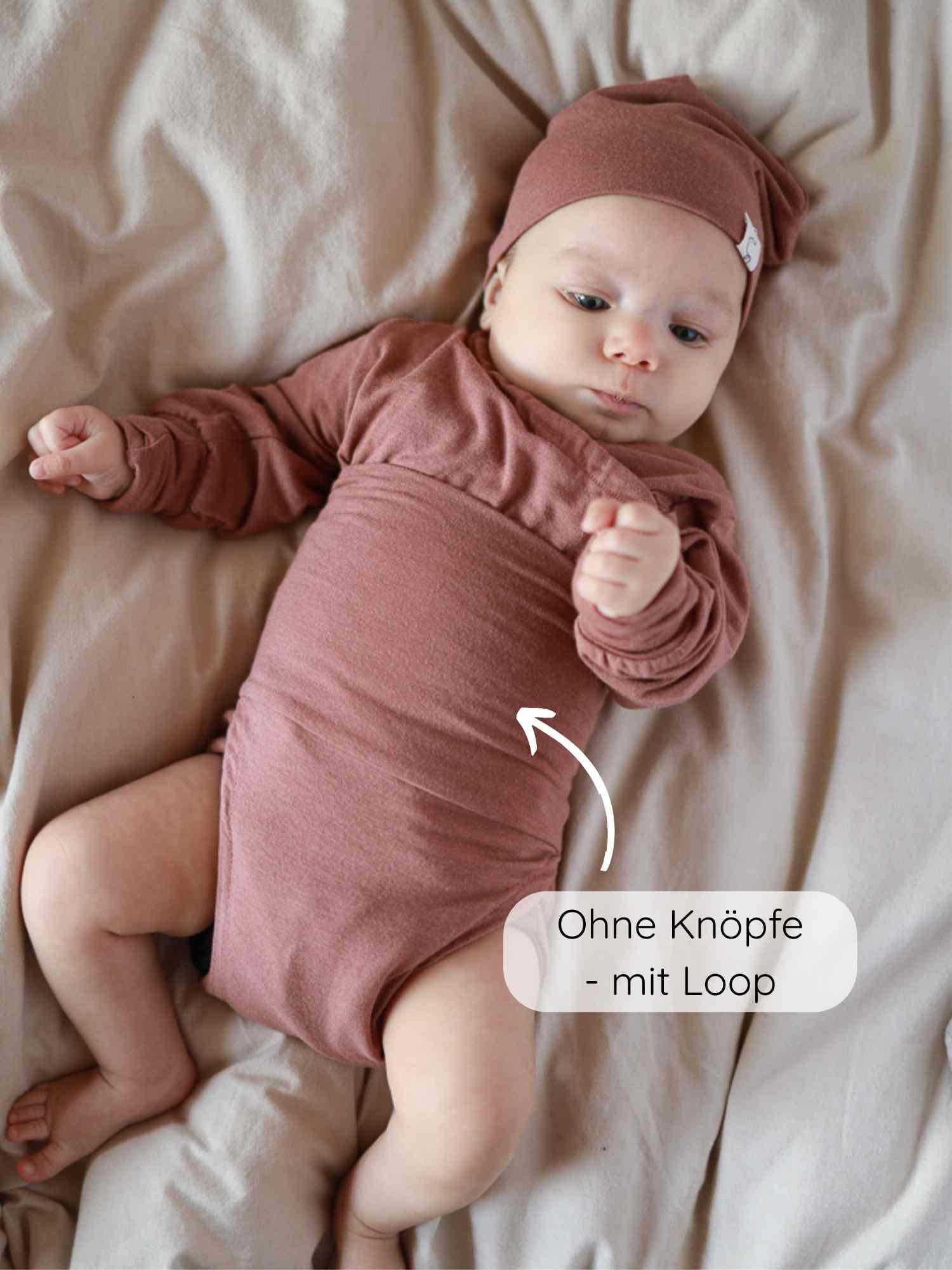 Kleines Baby in einem Loopbody Kaschmir-Mix - mitwachsender Babybody - Zimt, ohne Knöpfe, mit praktischem Loop für einfaches Anziehen und extra Wärme, aus hautfreundlichem Kaschmir-Modal-Mix, auf hellem Untergrund.