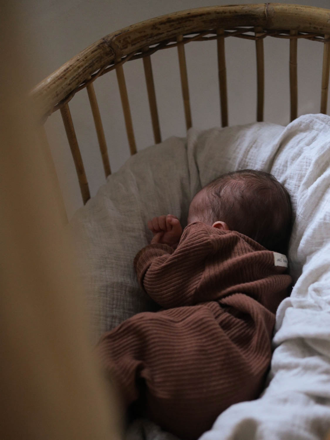 Baby in einem Kinderbett, eingehüllt in eine Decke, trägt den Mini Overall Rippstrick - Nougat aus recycelter Baumwolle, ideal für Komfort und Wärme, während es friedlich schläft. Erstausstattung Baby und Baby Geschenk zur Geburt.