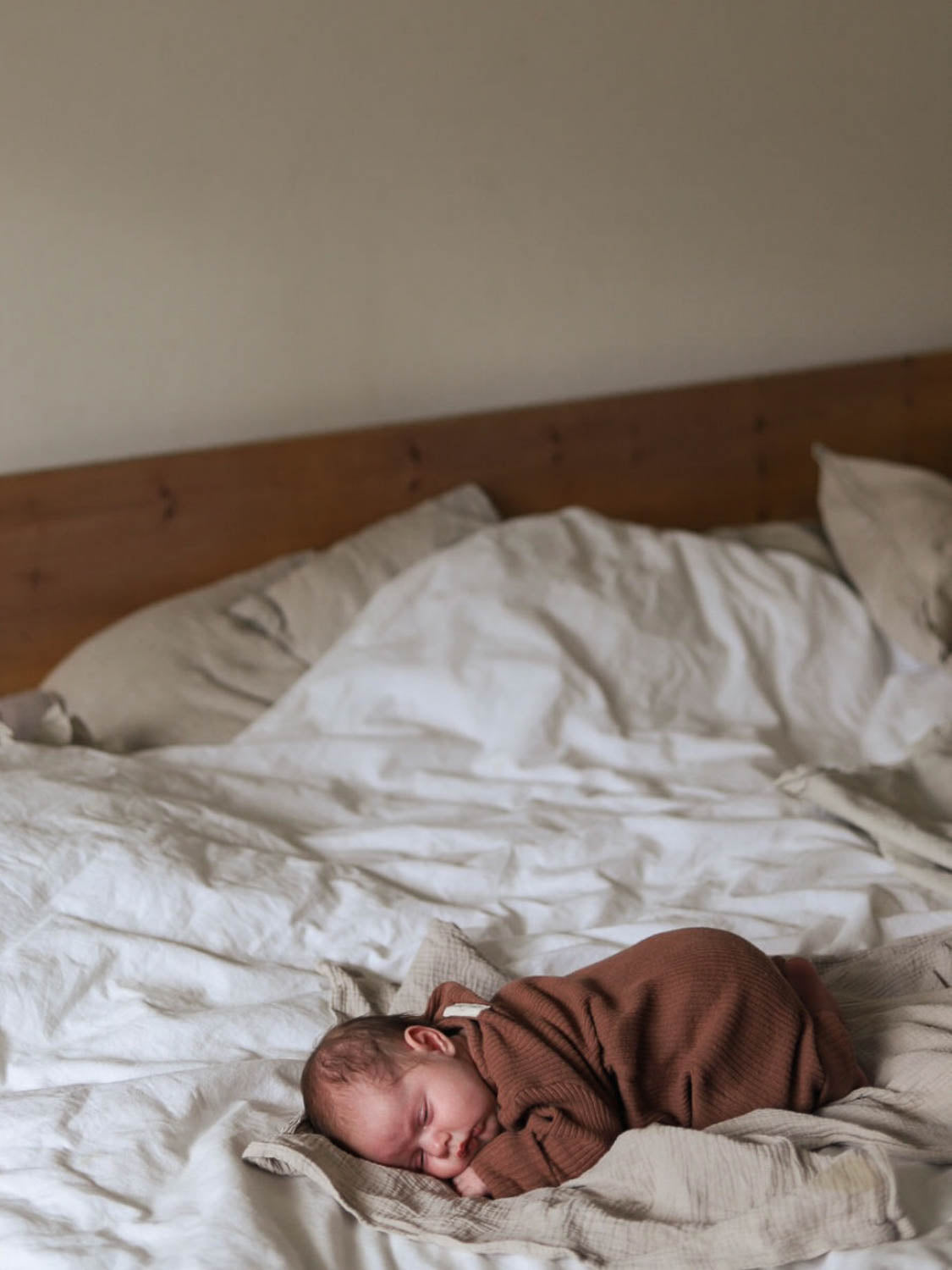 Mini Overall Rippstrick - Nougat: Ein Baby schläft auf einem Bett, eingekuschelt in den weichen, unisex Rippstrick-Overall, der aus recycelter Baumwolle gefertigt ist, für ganzjährigen Komfort und Wärme. Erstausstattung Baby und Baby Geschenk zur Geburt.