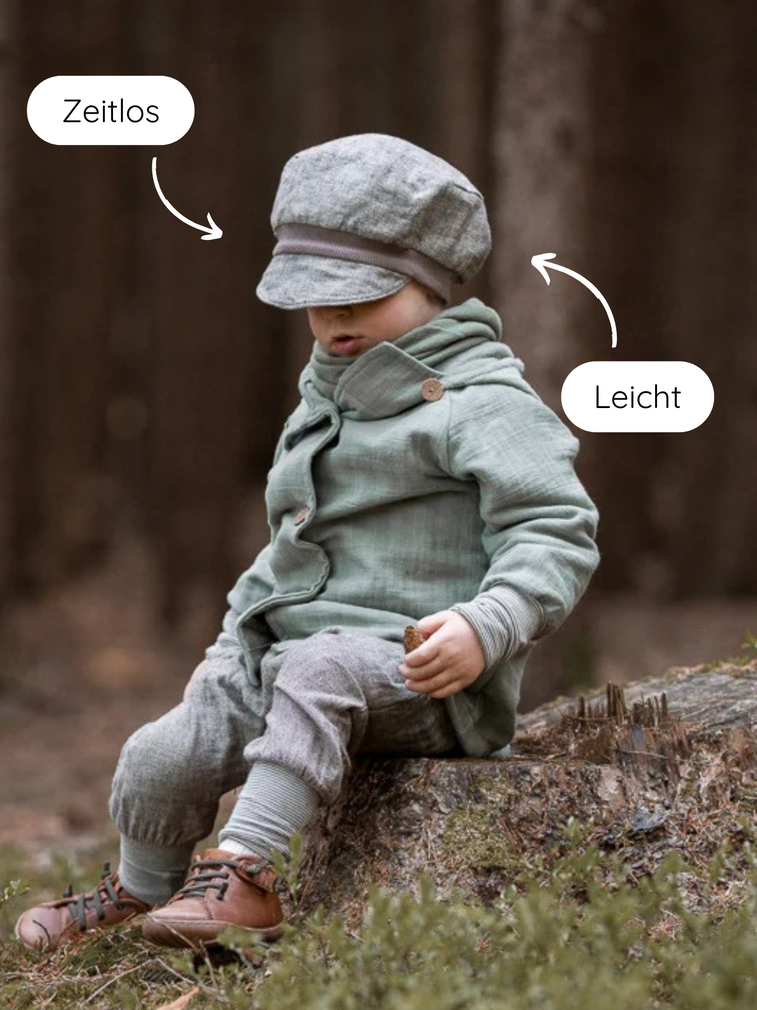 Kleinkind sitzt auf Baumstumpf, trägt Michelmütze Fischgrat Maus. Die Mütze aus Baumwoll-Fischgrat ist zeitlos und leicht, mit verstellbarem Zugband für optimalen Sitz. Hält einen kleinen Tannenzapfen.