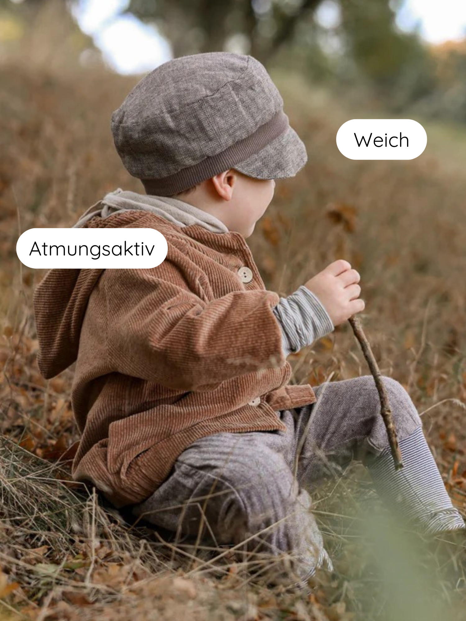 Kleinkind im Freien, trägt Michelmütze Fischgrat Maus mit kleinem Schirm. Kleidung atmungsaktiv und weich, betont durch deutsche Call-outs. Mütze sitzt sicher, ideal für Übergangszeit.