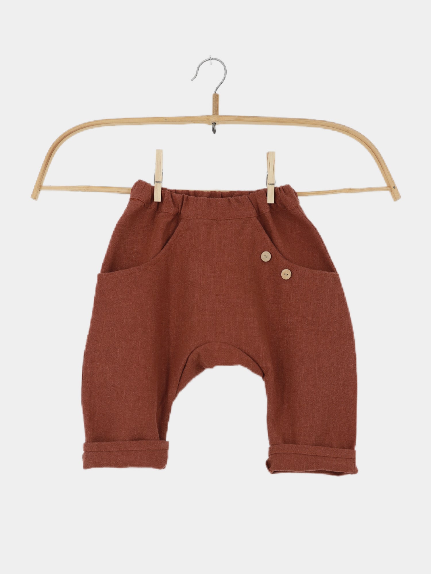 Sommerknicker Leinen - Ziegel: Kleine Kinderhose in Ziegelfarbe mit elastischem Bund, drop-crotch Schnitt, Bündchen an den Knöcheln, Fronttaschen und zwei dekorativen Holzknöpfen, aus leicht strukturiertem Leinenstoff.