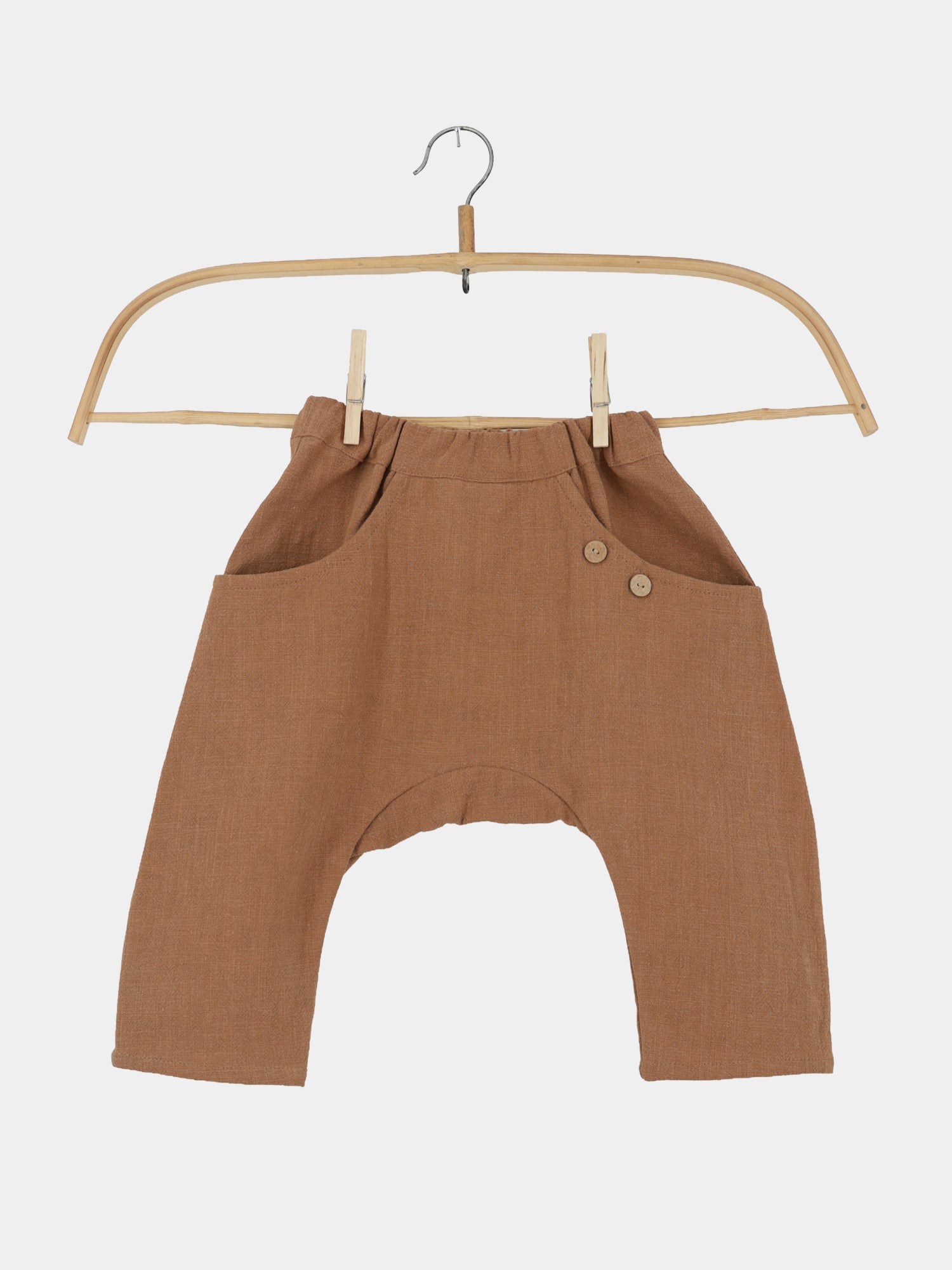 Sommerknicker Leinen - Weizen: Braune, drop-crotch Kinderhose aus 100% Leinen mit elastischem Bund, zwei Seitentaschen und dekorativen Knöpfen, auf Holzkleiderbügel vor weißem Hintergrund gezeigt.