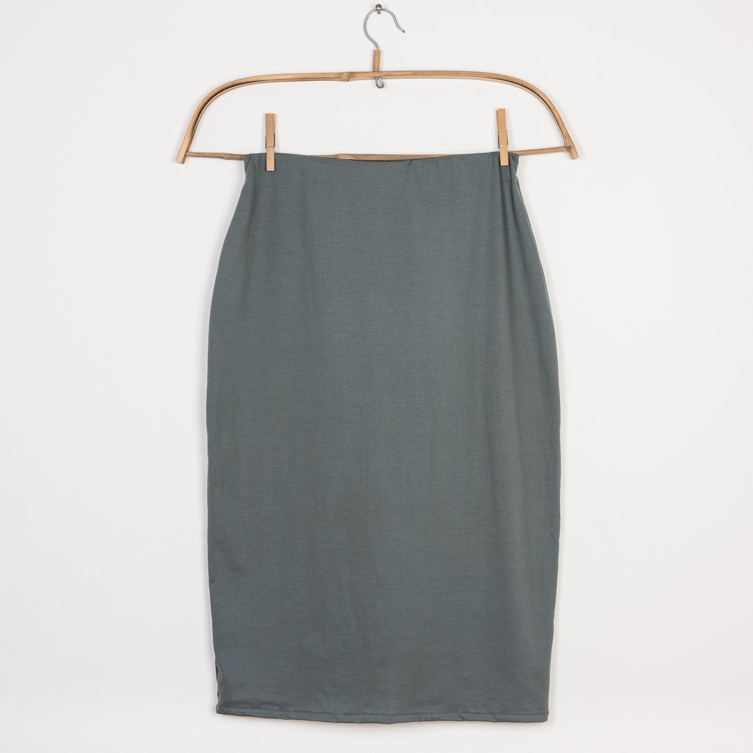 Der Bleistiftrock Jersey Taube Gr. L hängt an einem Holzbügel mit Clips, zeigt einen geraden Schnitt und reicht bis zur Mitte der Wade, ideal für elegante und schlichte Outfits.