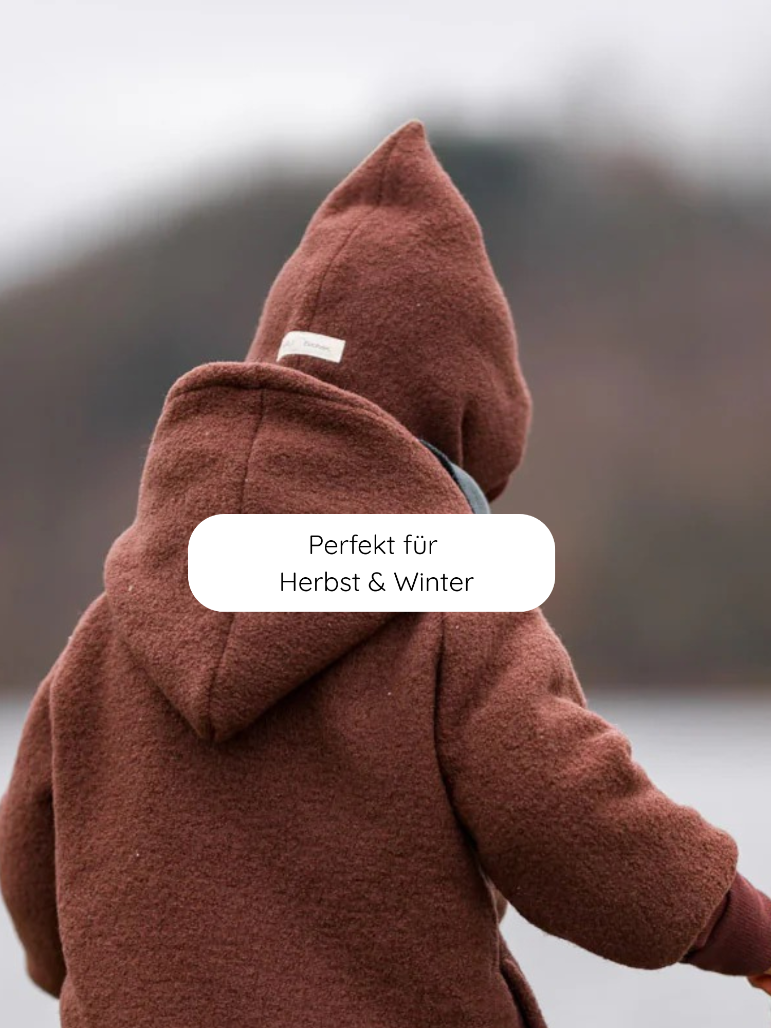 Ein Kind trägt die Schlupfmütze Wollwalk - Schoko mit spitzer Kapuze, ideal für kalte Tage. Perfekt für Herbst und Winter, bietet sie Schutz und Komfort von Kopf bis Hals.