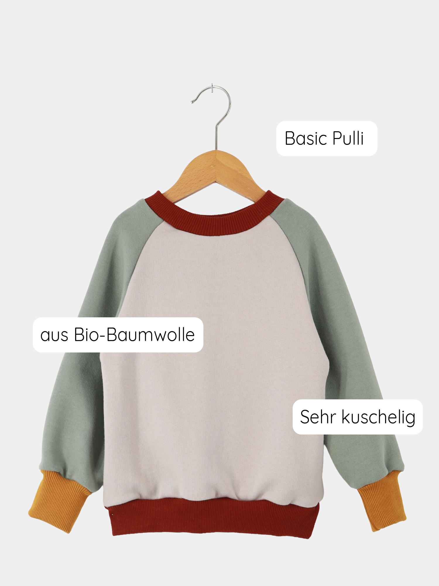 Upcycling-Pulli Bio-Sweat - Farbenzauber: Kinder-Sweatshirt mit Raglanärmeln, aus Bio-Baumwolle. Sanfte Farbkombinationen, nachhaltig aus Stoffresten gefertigt, präsentiert auf einem Holzkleiderbügel.