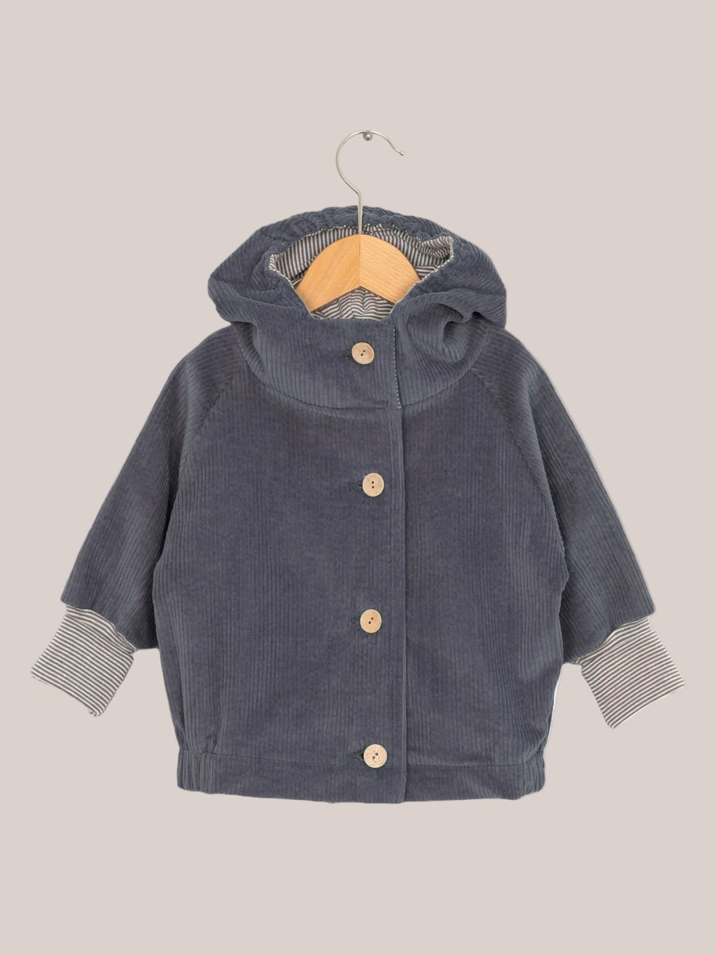 Wichteljacke Breitcord - Denim auf einem Holzbügel, mit Ringel-Armbündchen und Wichtelkapuze, aus weichem Cord für komfortables Tragen, handgefertigt in Deutschland.