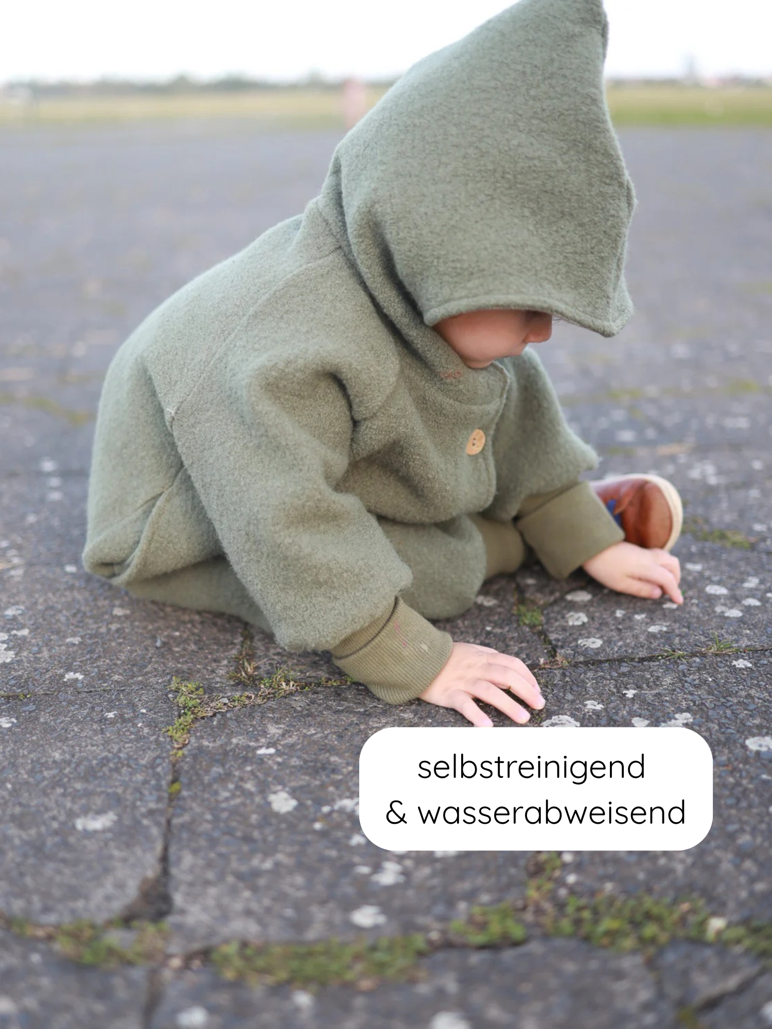 Kleinkind in mossgrüner Wichteljacke Wollwalk - Pistazie mit spitzem Kapuzenhut und Holzknopf. Hinweis: selbstreinigend & wasserabweisend. Ideal für Herbst, Winter, Frühling, gefüttert mit Bio-Jersey.