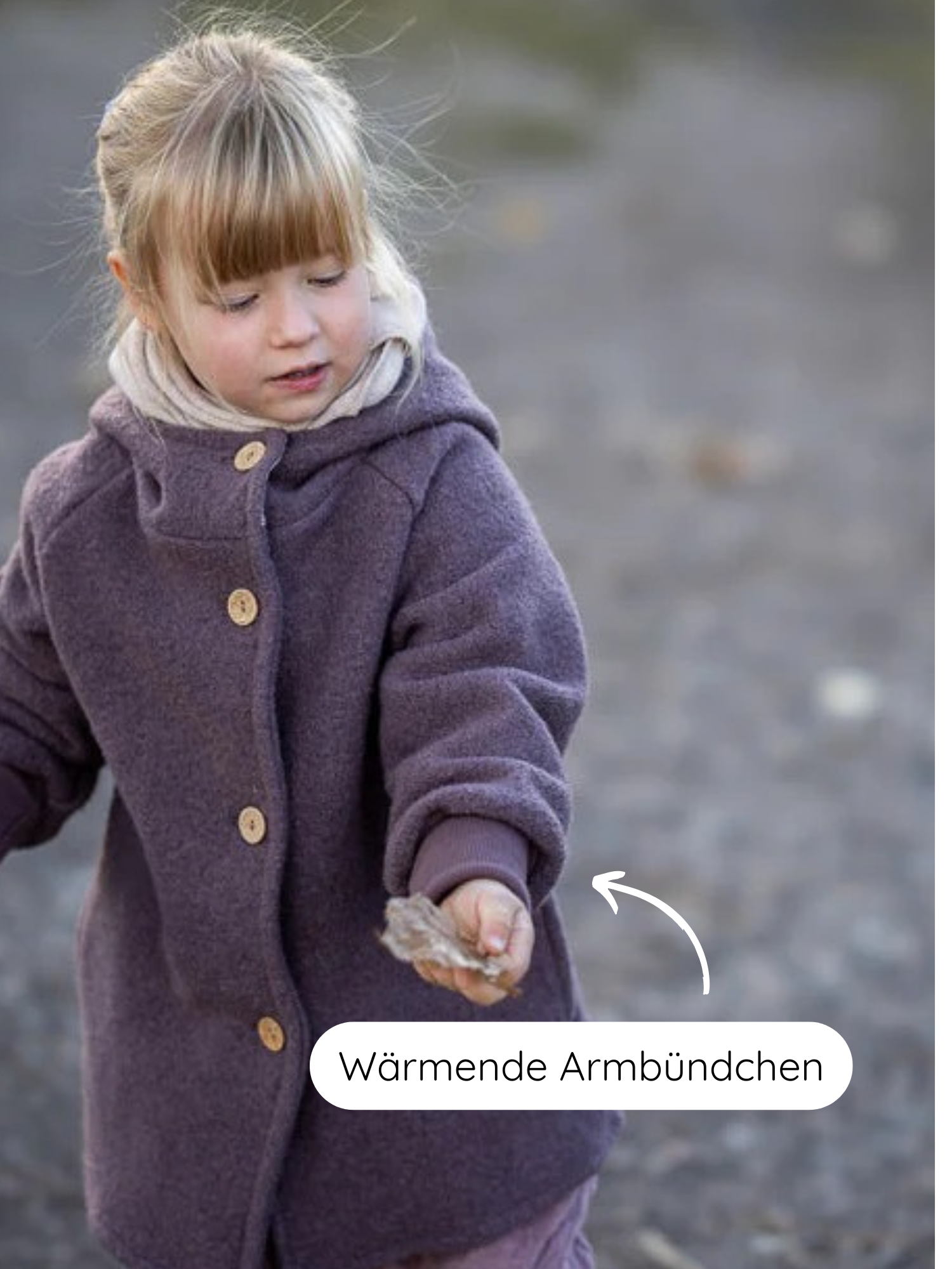 Ein Mädchen trägt die Wichteljacke Wollwalk - Malve mit Kapuze und wärmenden Armbündchen. Sie hält ein Blatt, während ein Pfeil auf den Ärmel zeigt, der Komfort und Wärme bietet.