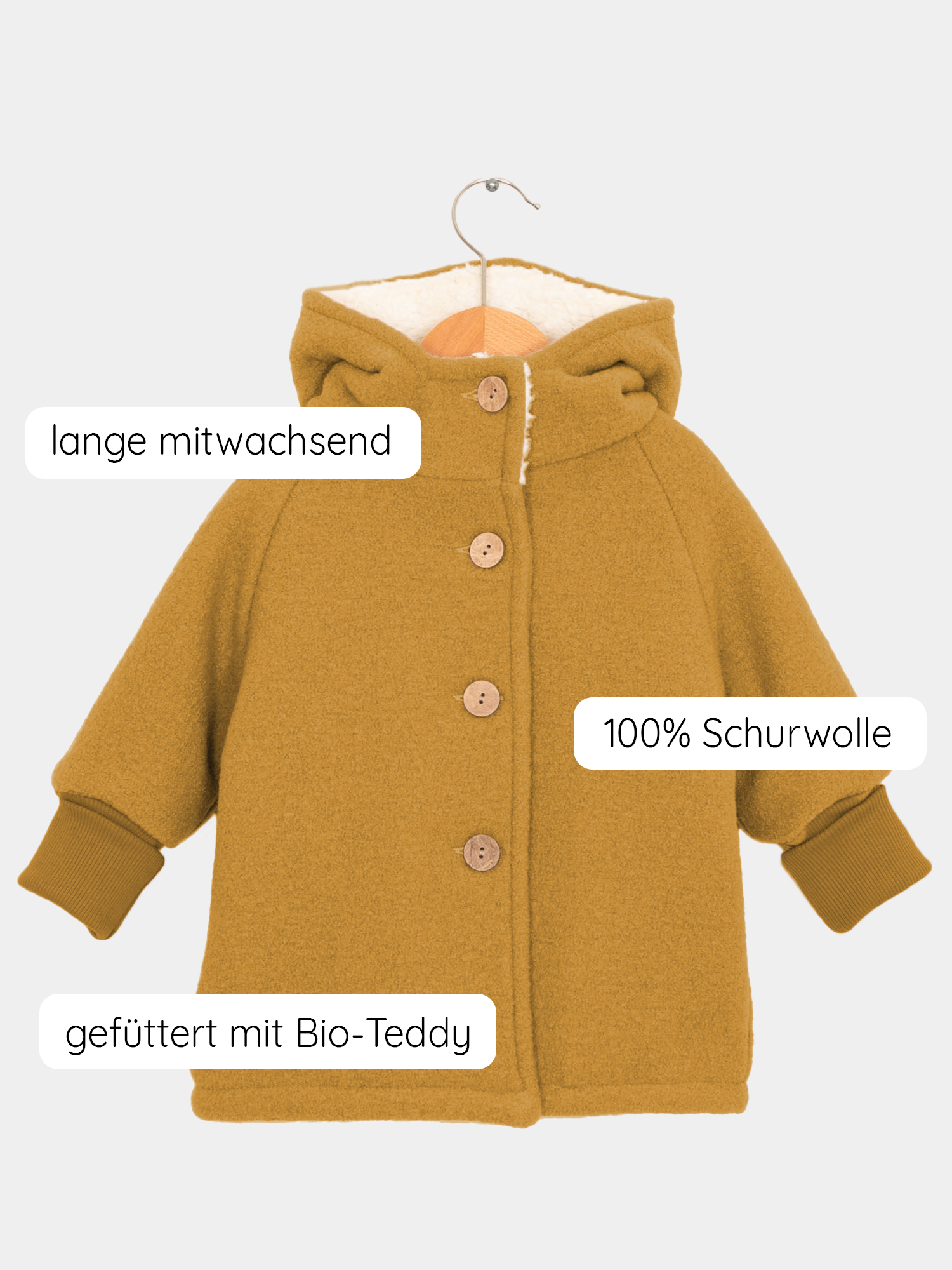 Teddy-Wichteljacke Wollwalk - Honig: Kinder-Mantel aus 100 % Schurwolle, mit Holzknöpfen, verstellbarer Länge, und Bio-Teddyfutter. Auf einem Holzkleiderbügel, zeigt breite Krempelbündchen und spitze Kapuze.